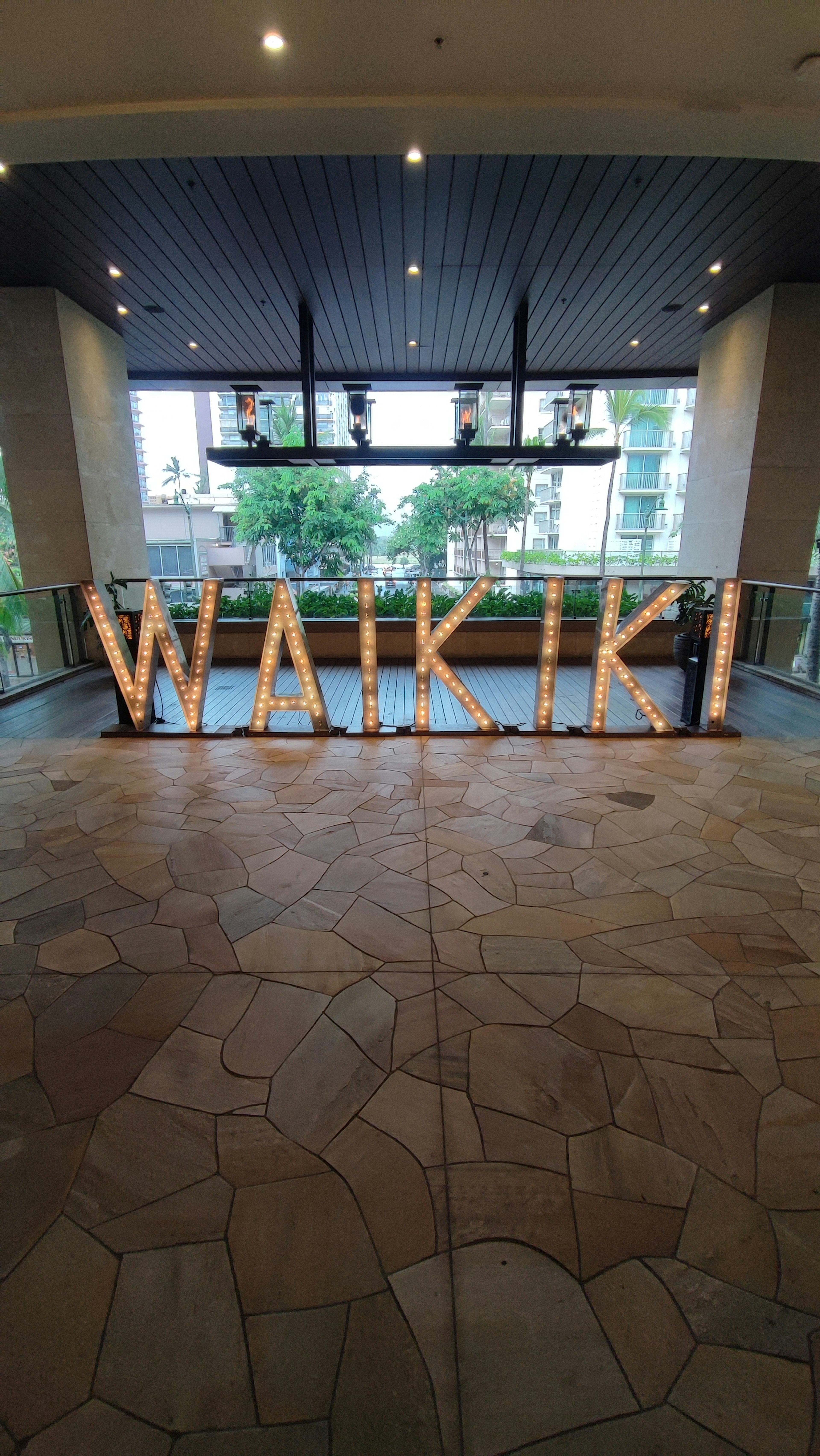 Cartel iluminado de WAIKIKI en la entrada de un hotel con piso de piedra