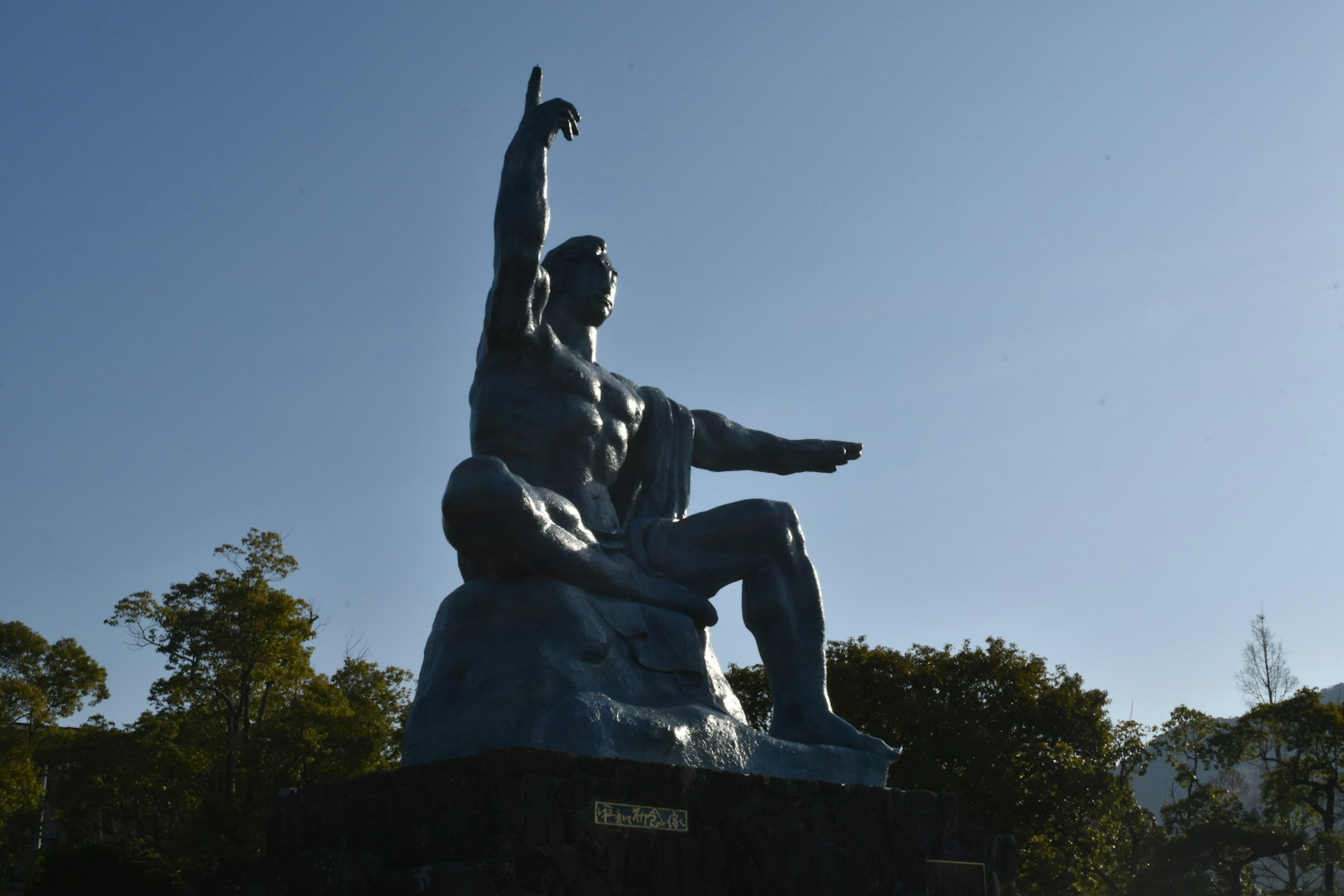 Une sculpture puissante sous un ciel bleu représentant un homme avec une main levée et l'autre tendue vers l'avant