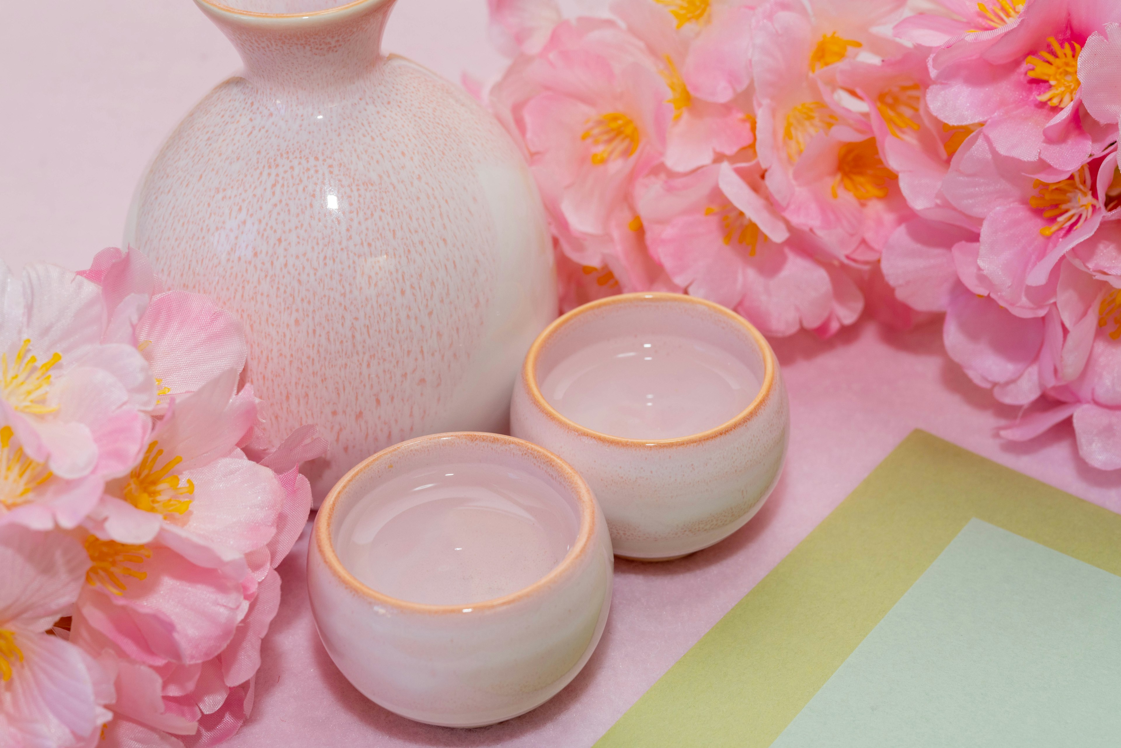 Flores rosas delicadas con una botella de sake de cerámica blanca y dos tazas pequeñas