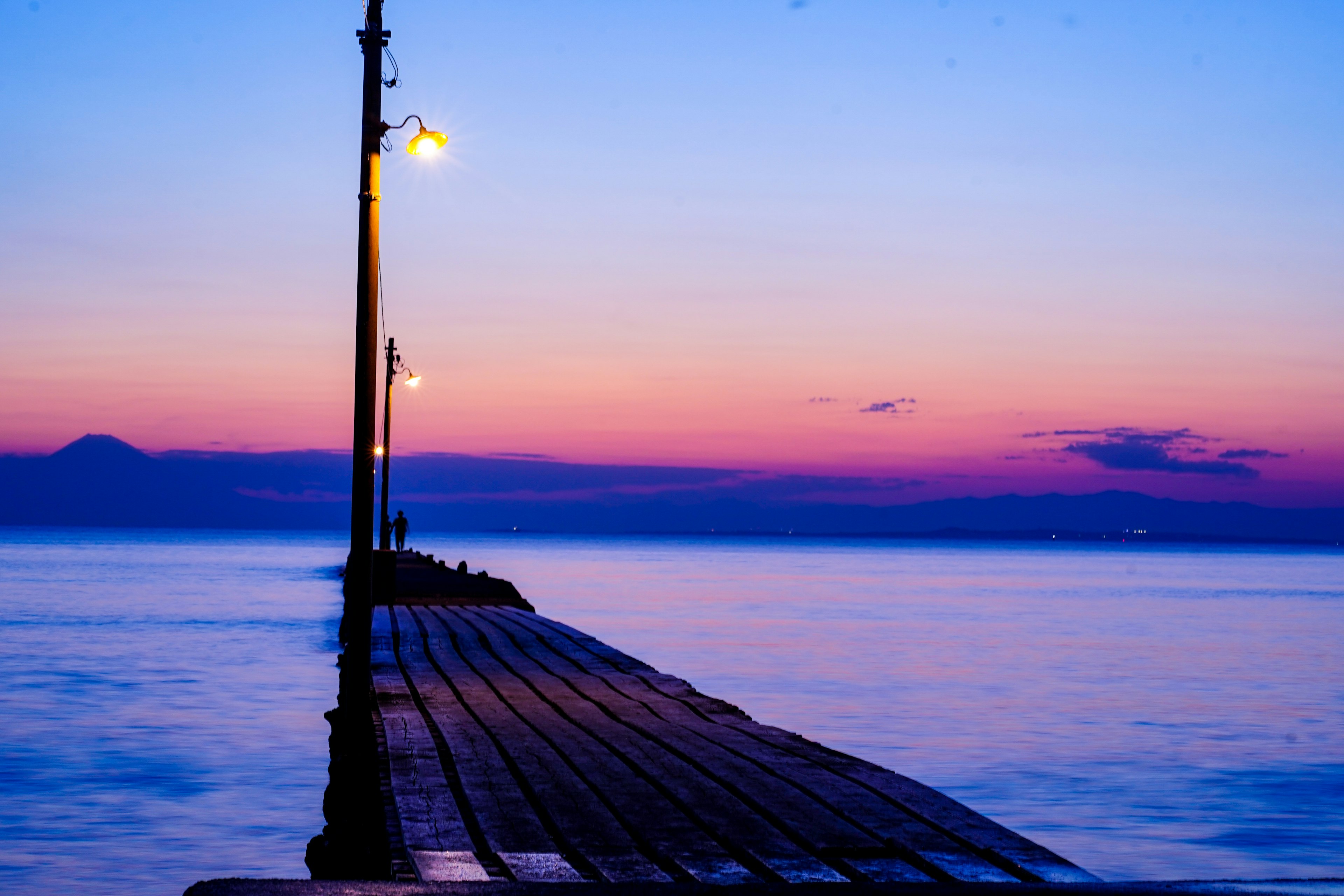 Steg, der ins Meer führt bei Sonnenuntergang mit Straßenlaternen