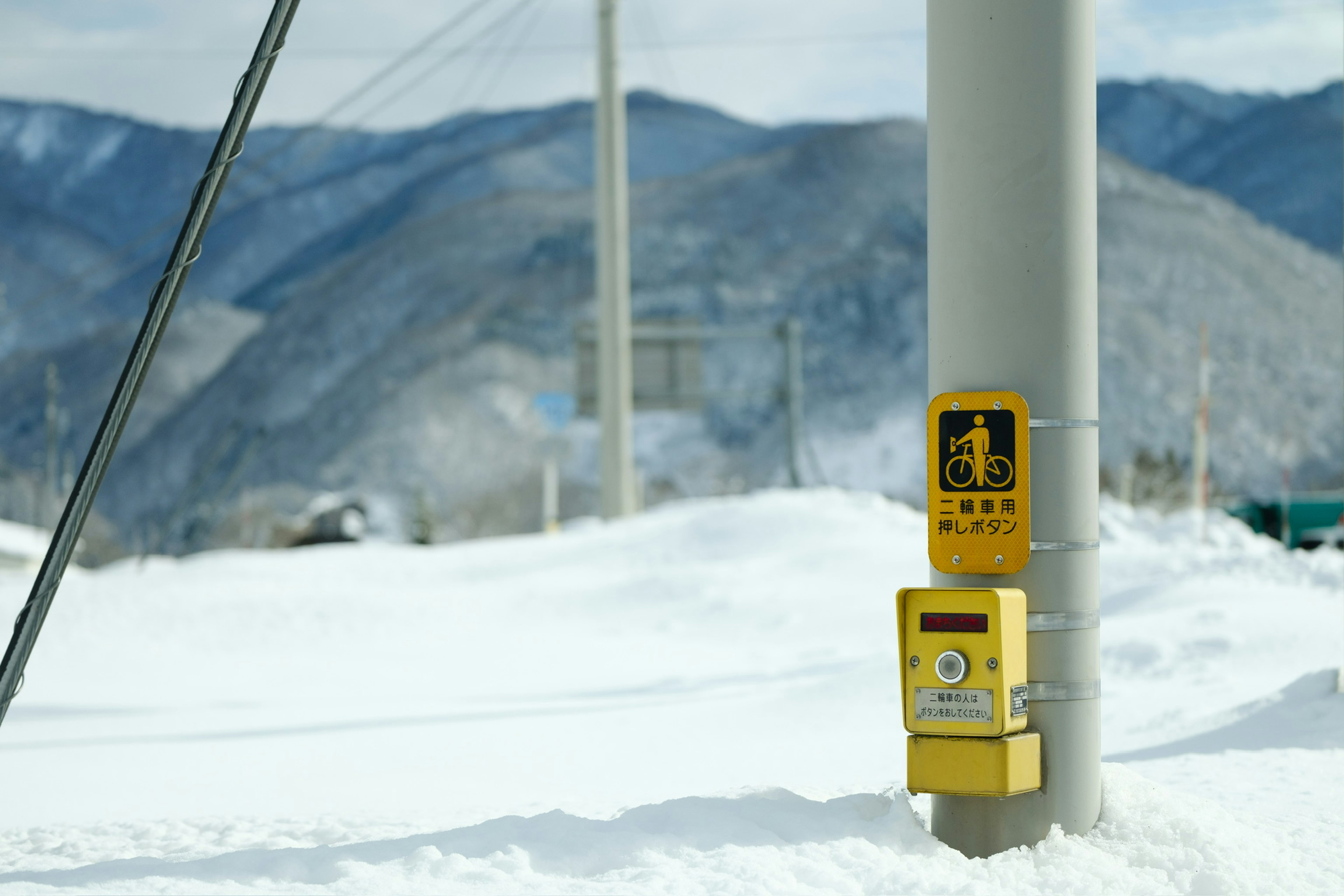 A yellow traffic signal and box standing in a snowy landscape