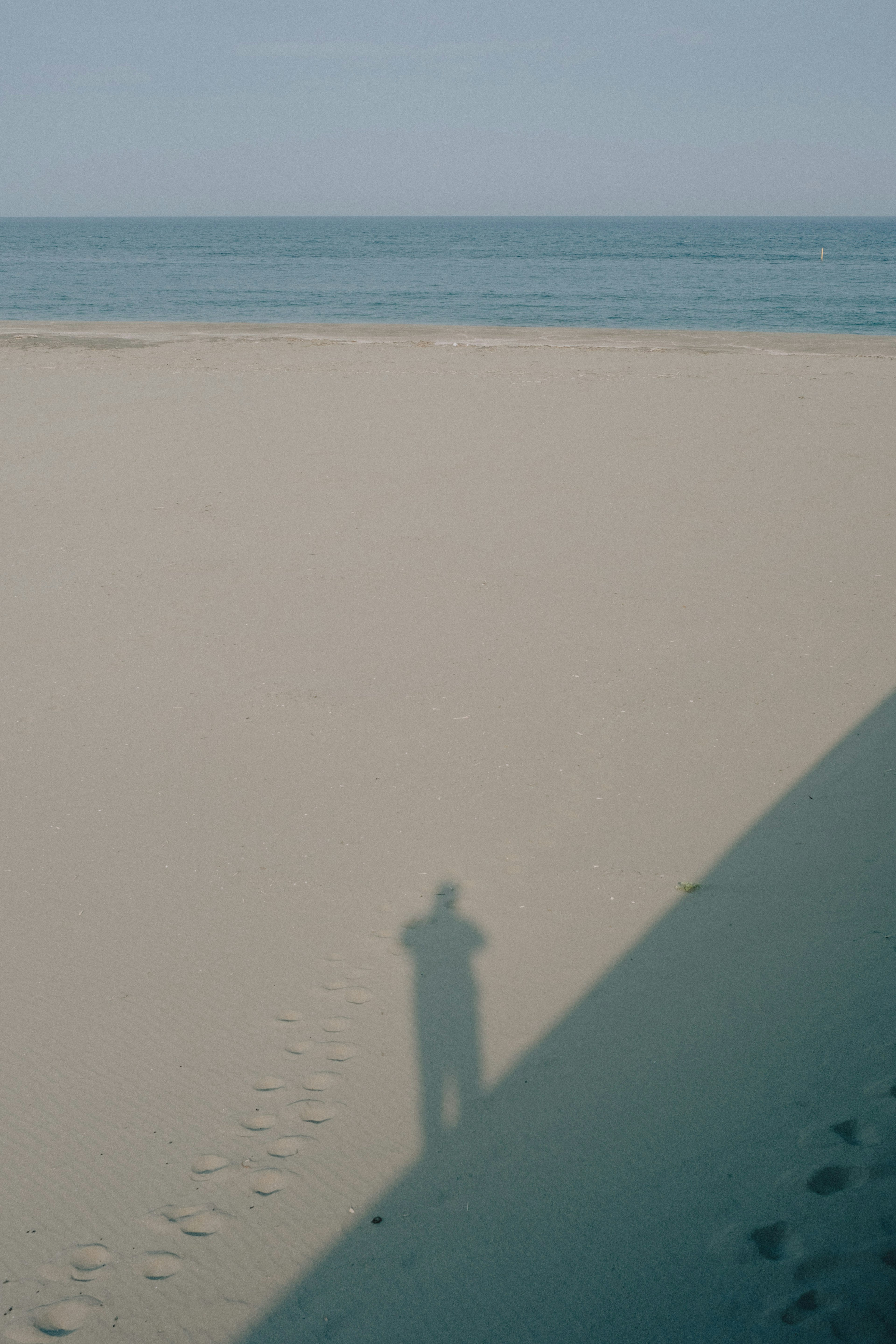 Schatten einer Person am Strand mit ruhigem Meer im Hintergrund