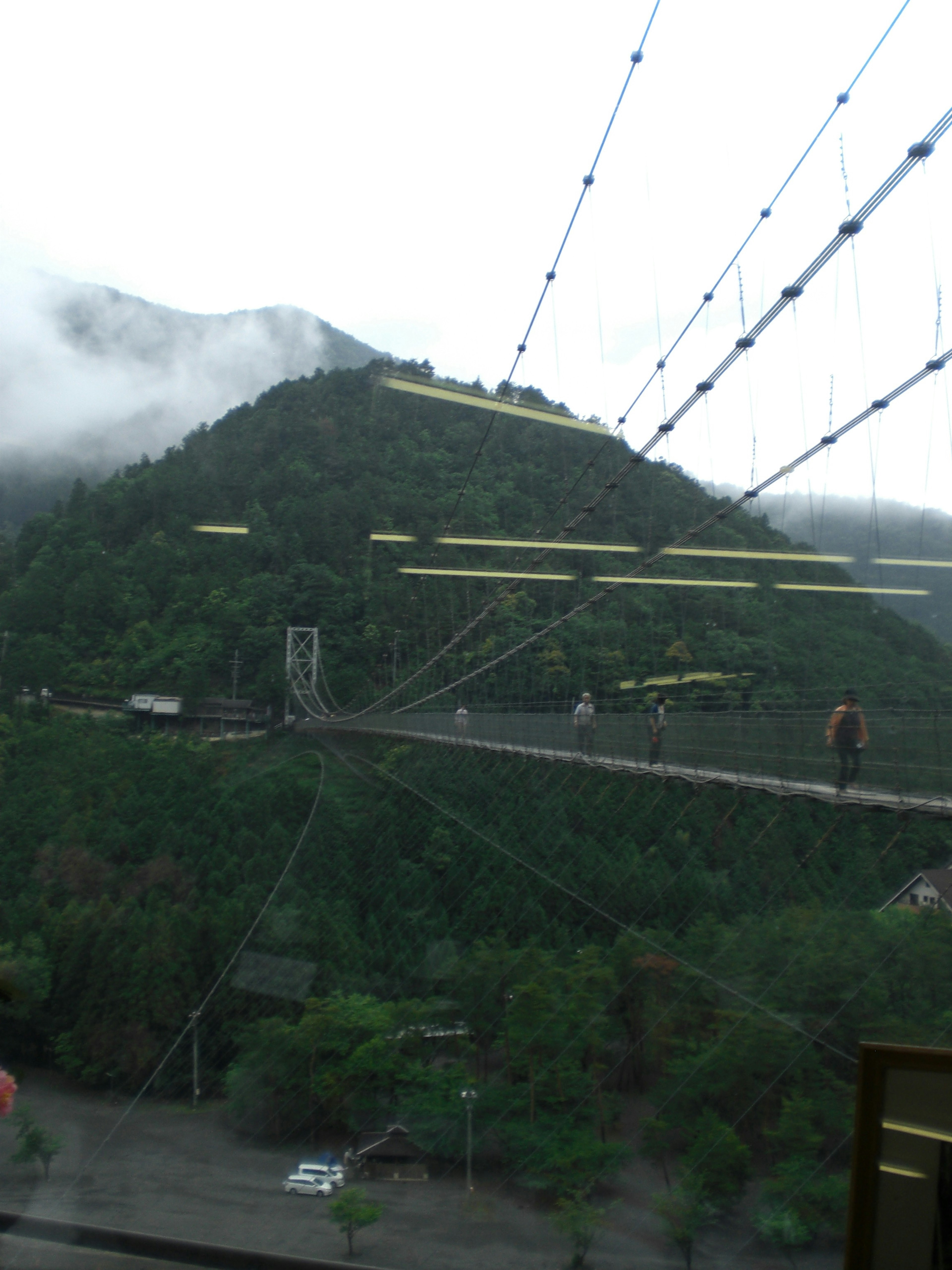 Vue panoramique d'une montagne couverte de nuages avec un pont suspendu et des personnes dessus