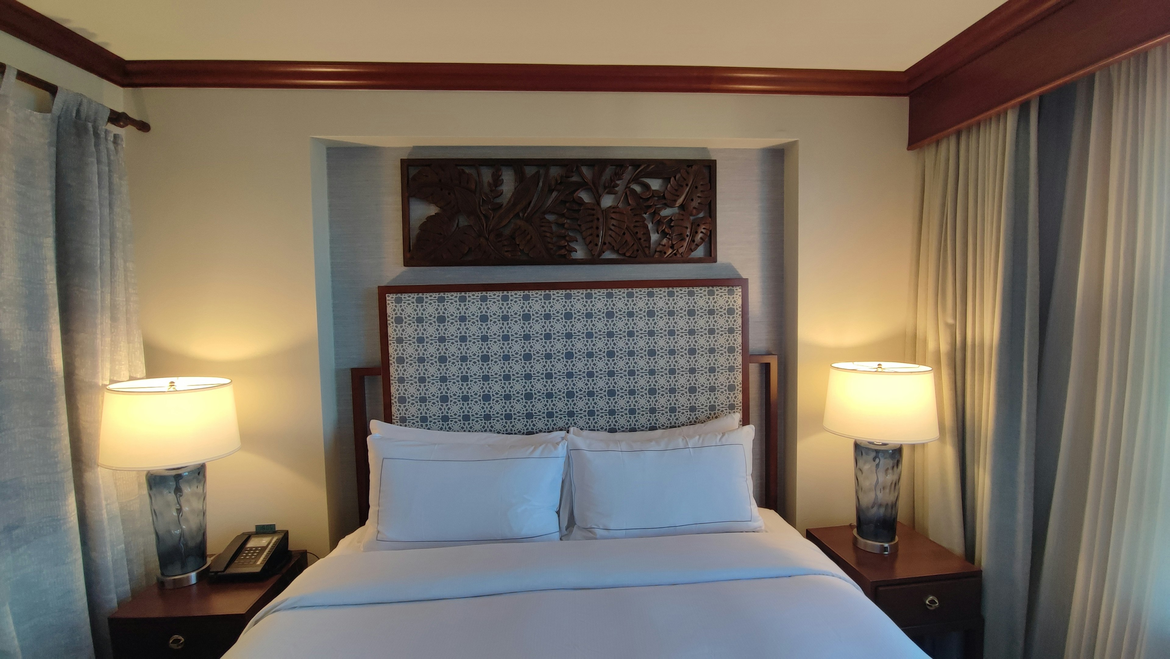 Hotel room featuring a bed with decorative headboard lamps and curtains