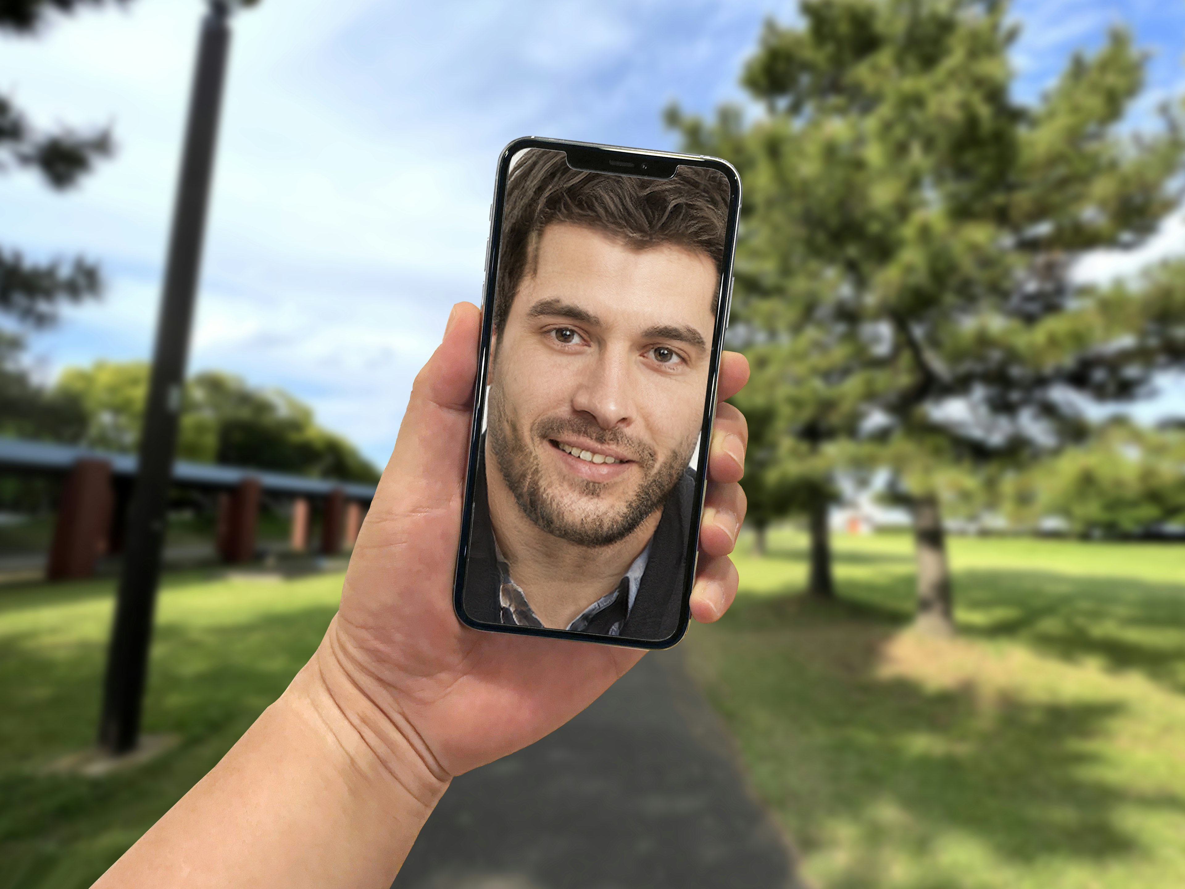 Una persona che tiene uno smartphone con il volto sorridente di un uomo in un parco