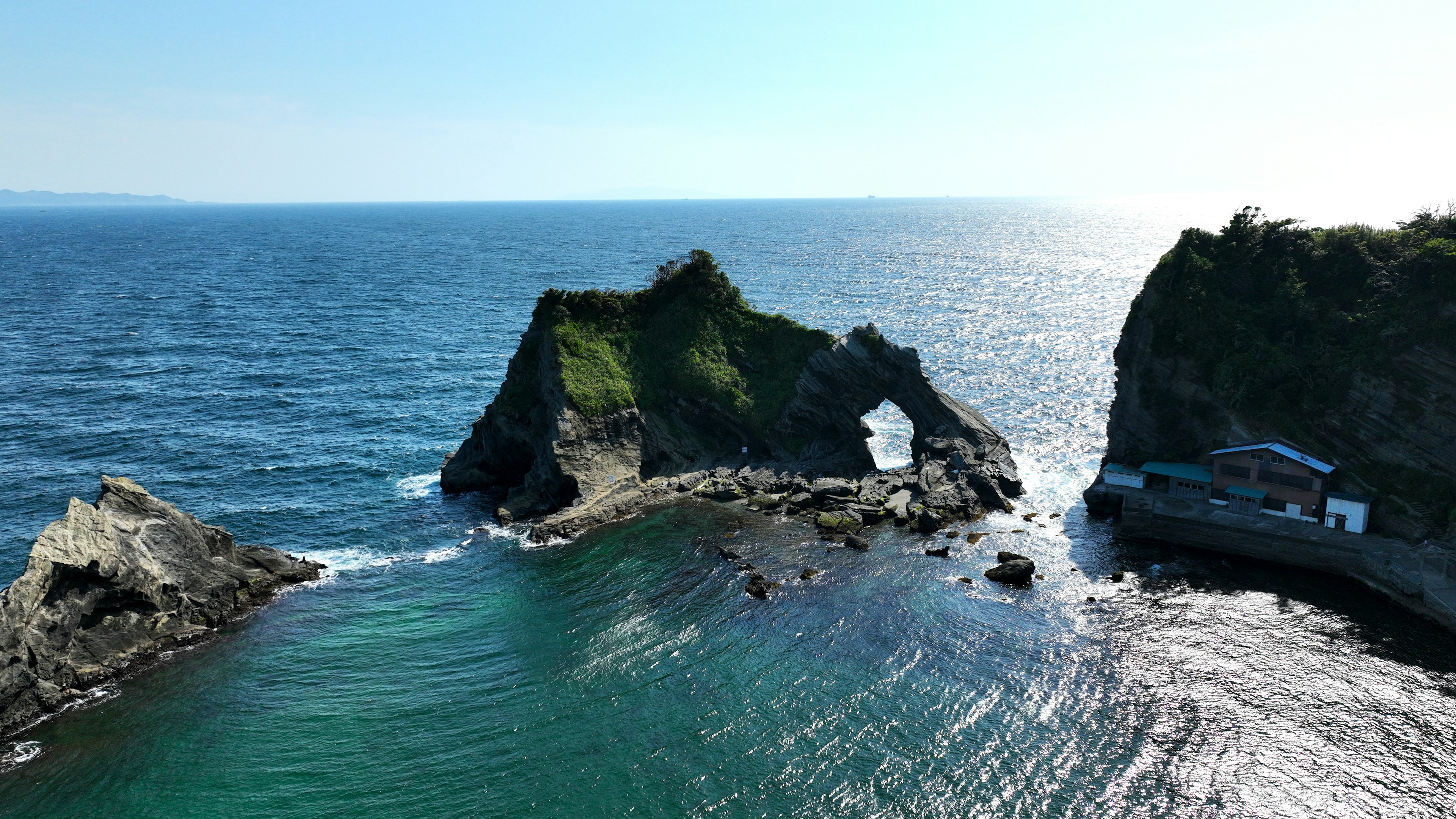 Natural rock arch between blue sea and green hills