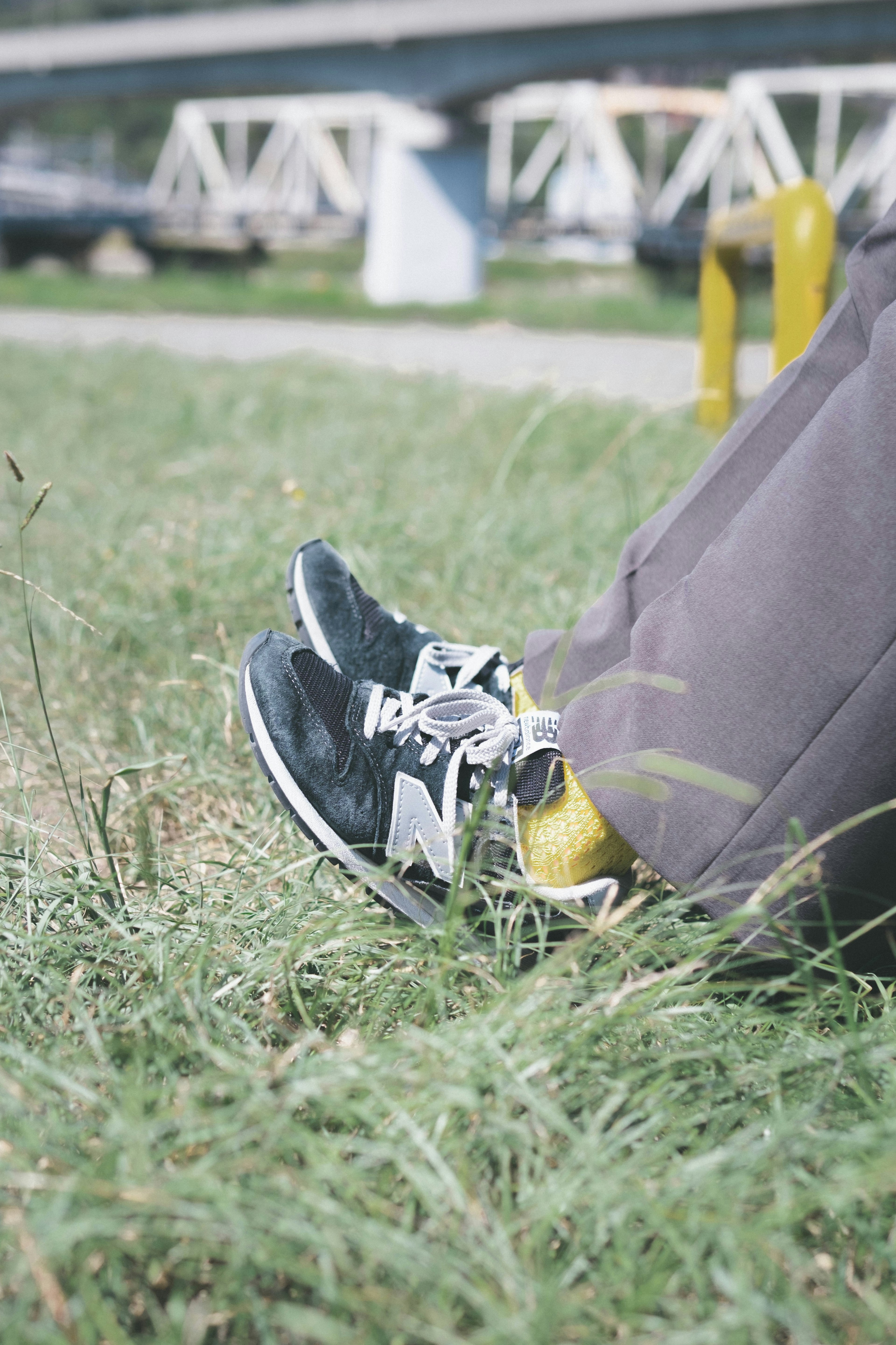 Close-up of black New Balance sneakers on grass with a person sitting