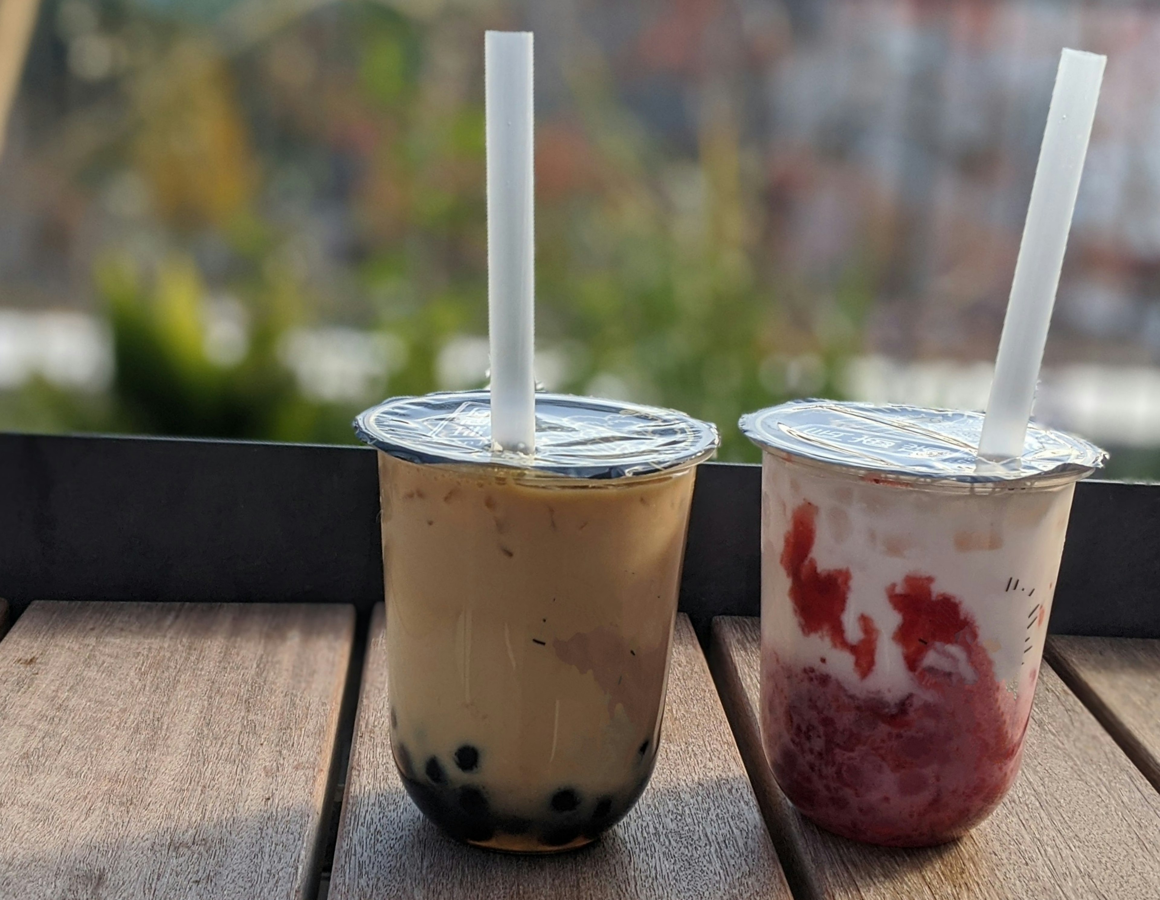 A photo of two drinks on a wooden table one is iced coffee with tapioca pearls and the other is a strawberry drink