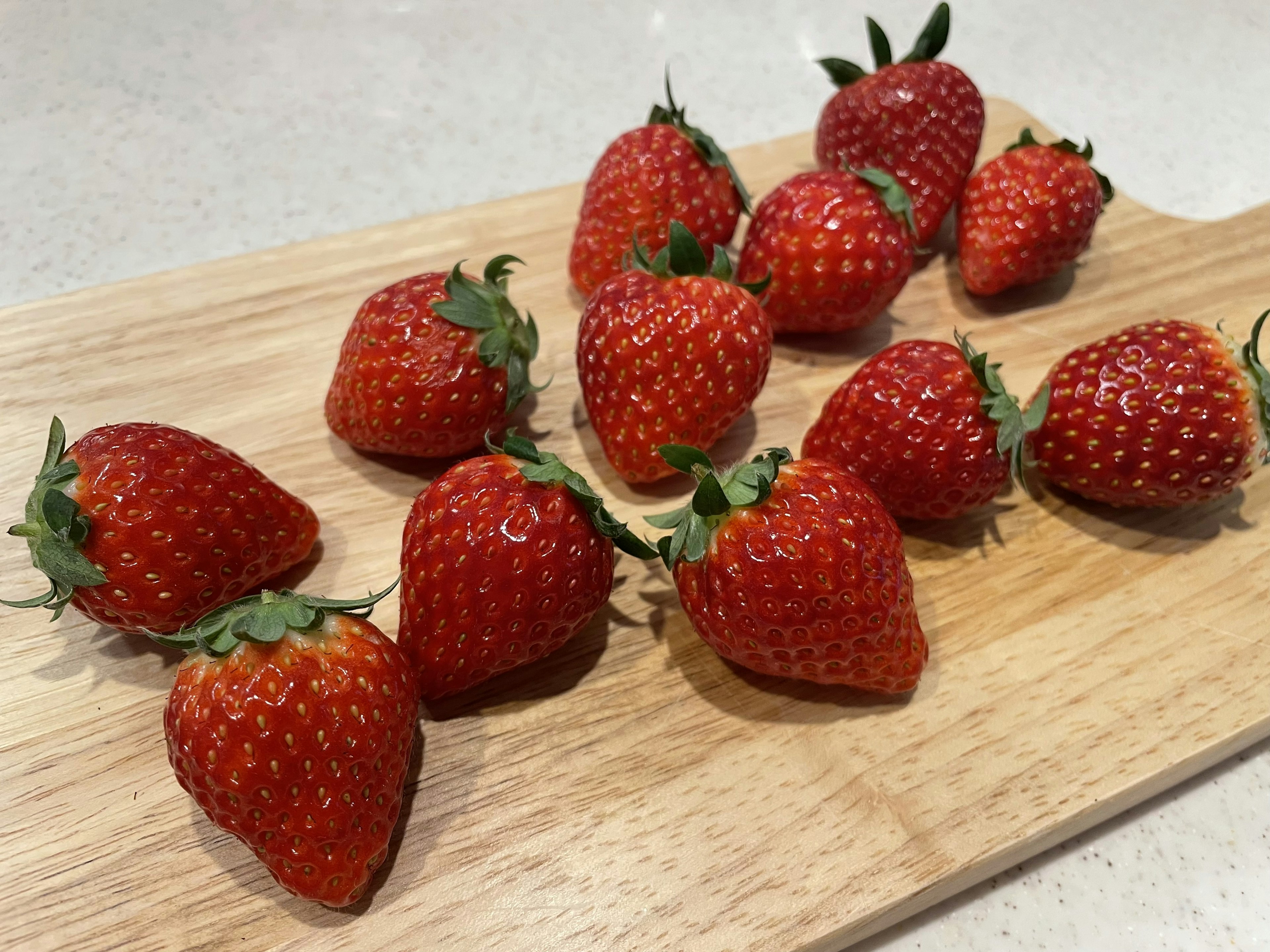 Twelve fresh strawberries arranged on a wooden board