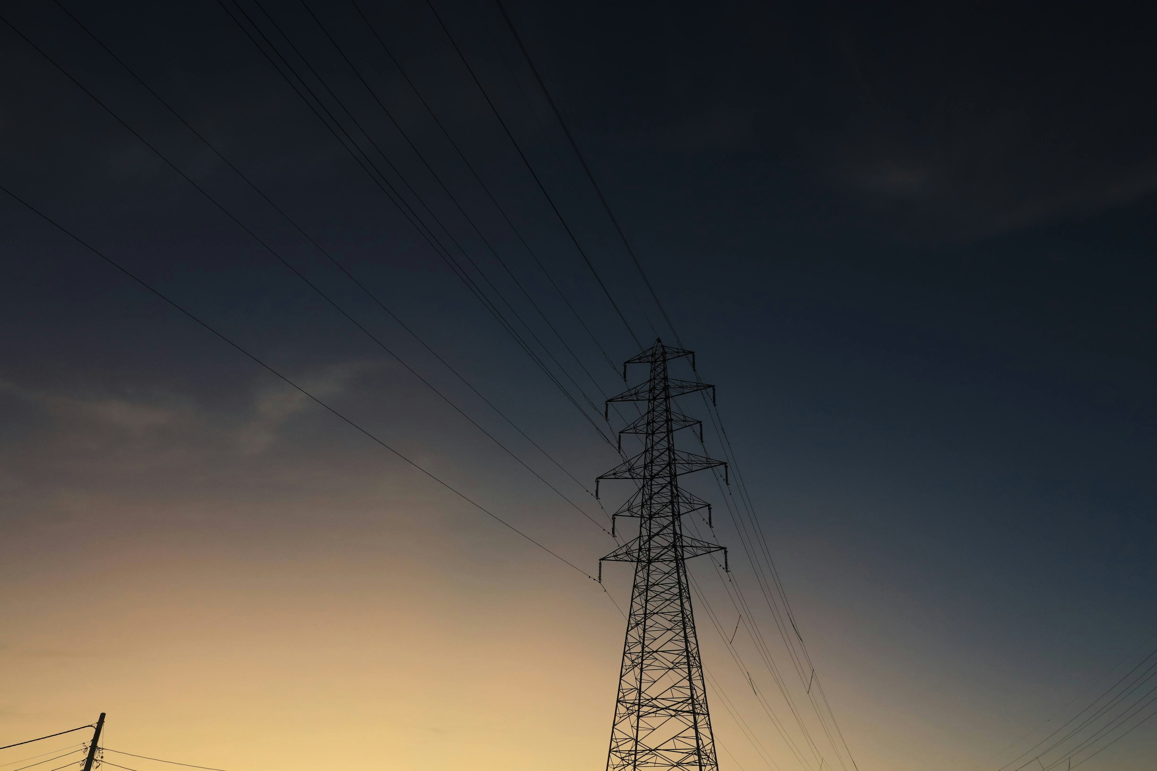 Silhouette de una torre eléctrica contra un cielo oscureciéndose al atardecer