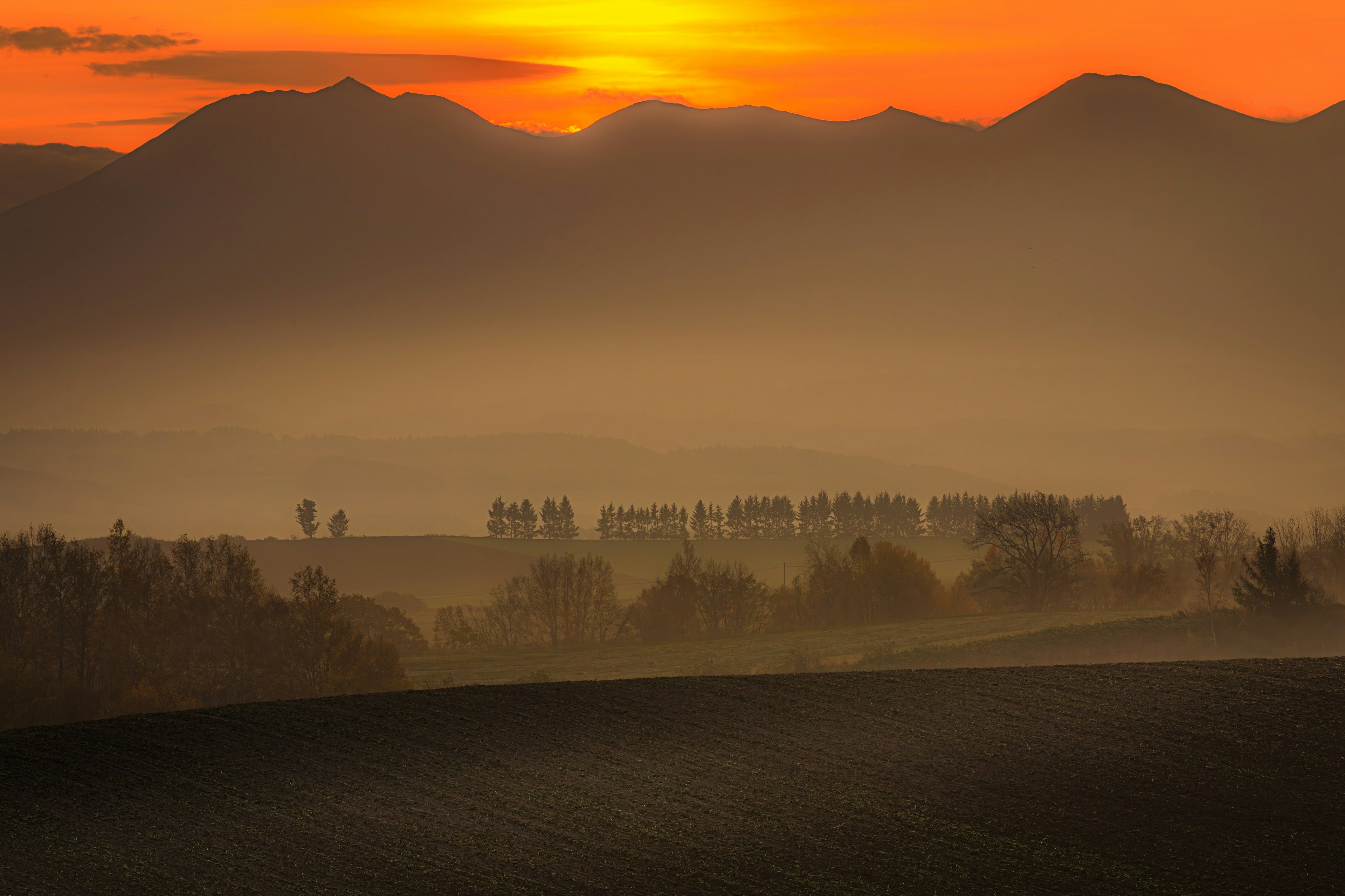 Landschaft mit Sonnenuntergang hinter Bergen nebligen Hügeln und Baum-Silhouetten