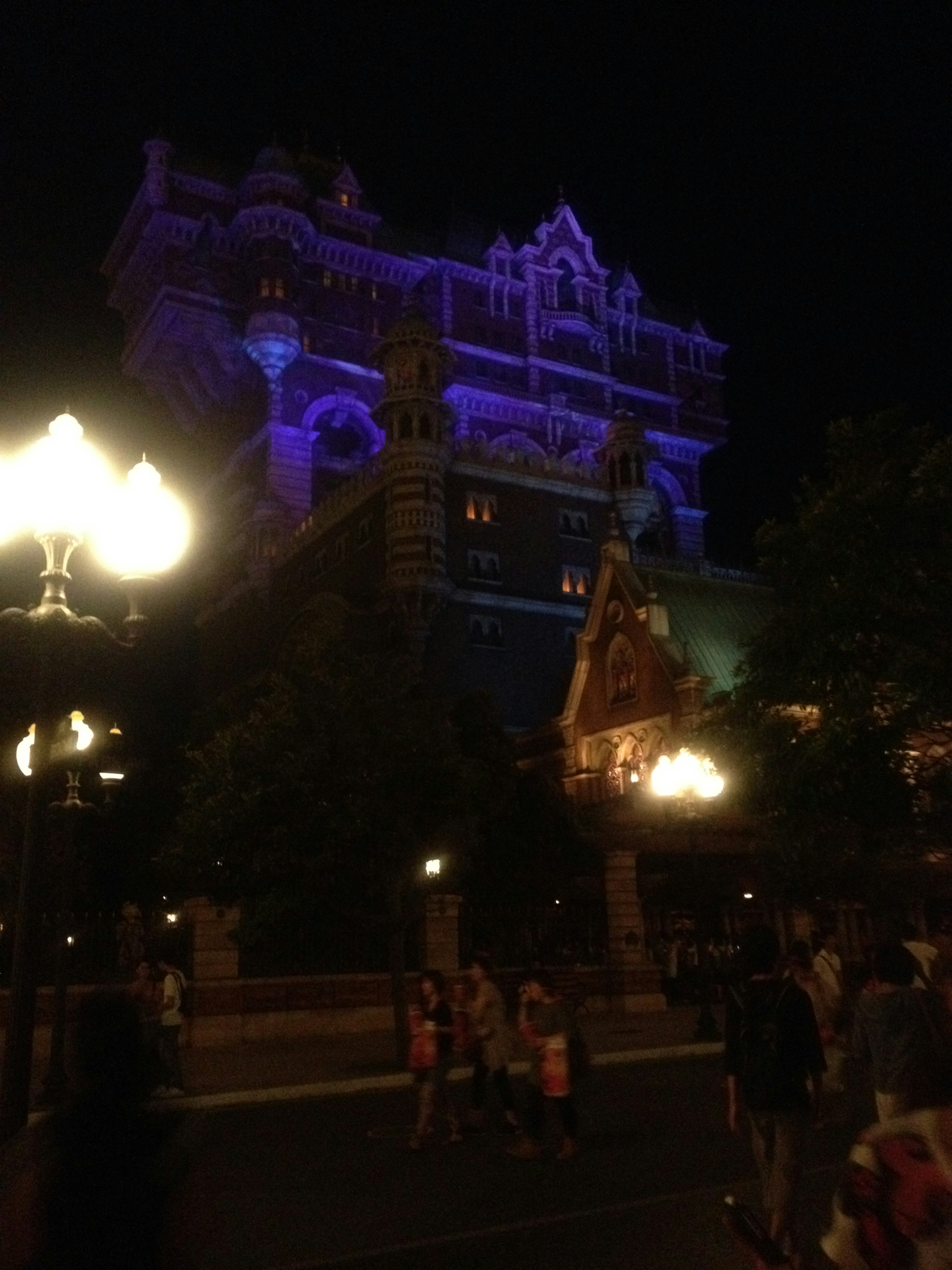 Fantastical building illuminated in purple at night with people walking nearby