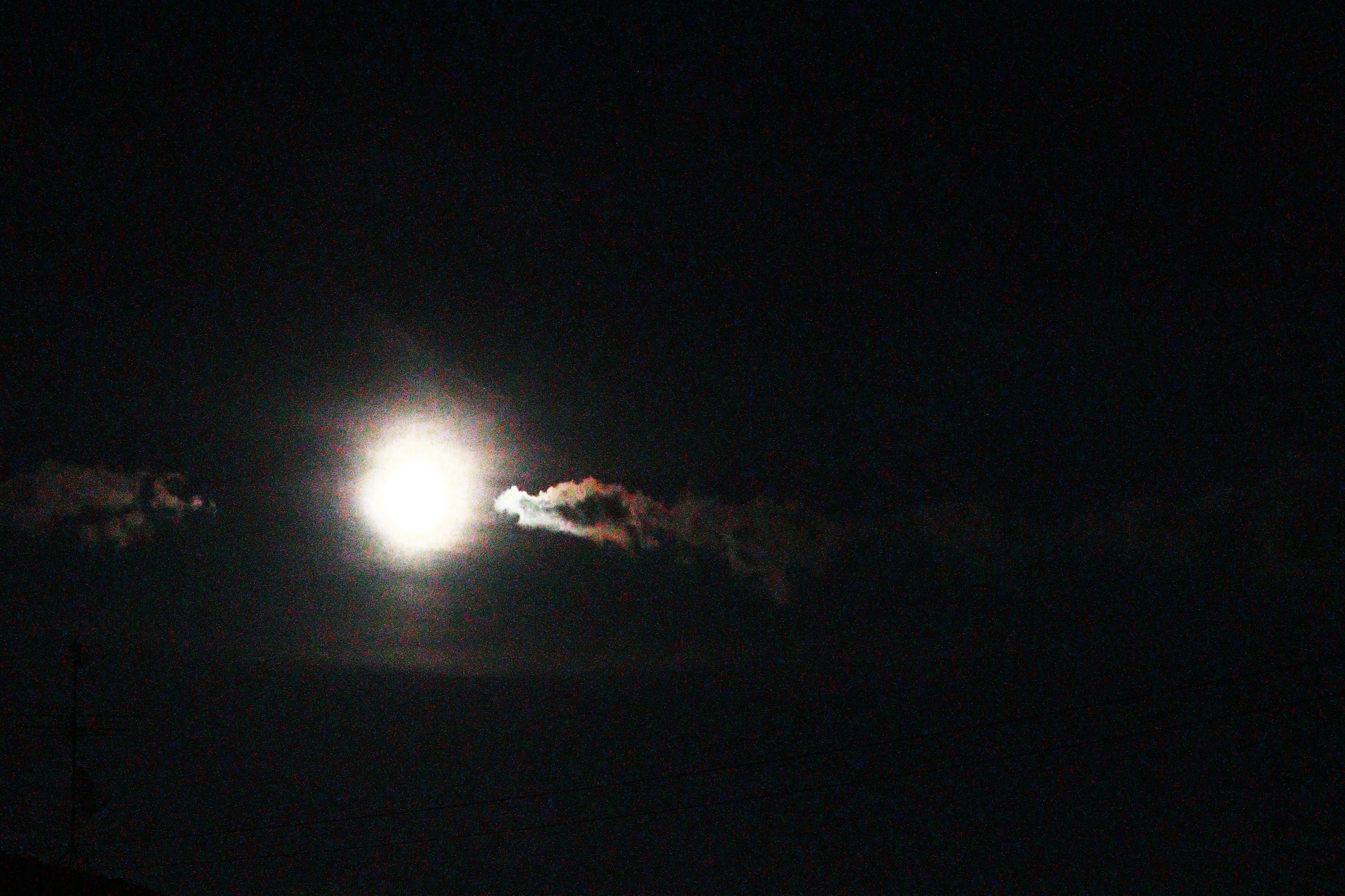 Bright moon in the night sky partially obscured by clouds