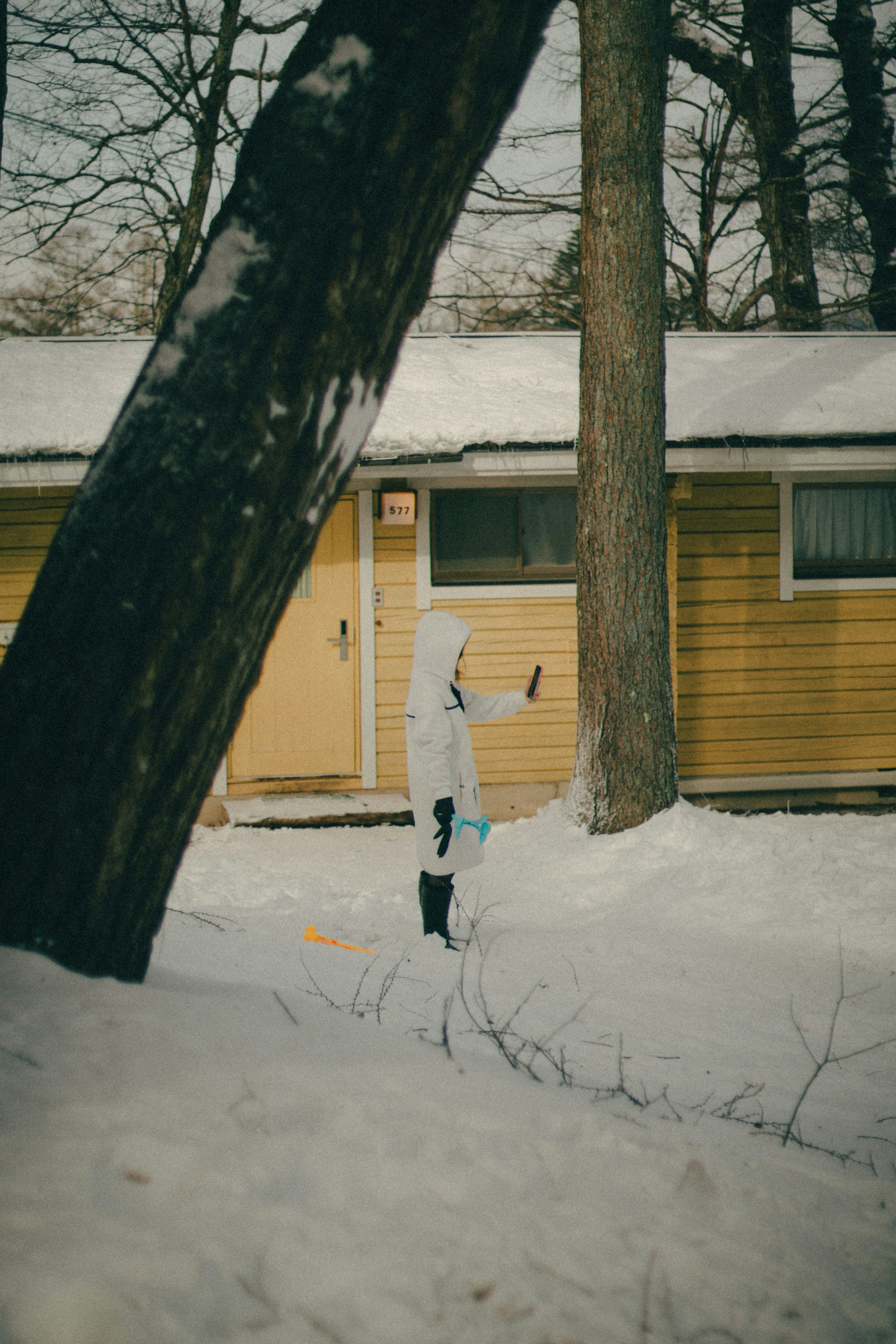 雪の中で白い服を着た子供が立っている背景に黄色い小屋