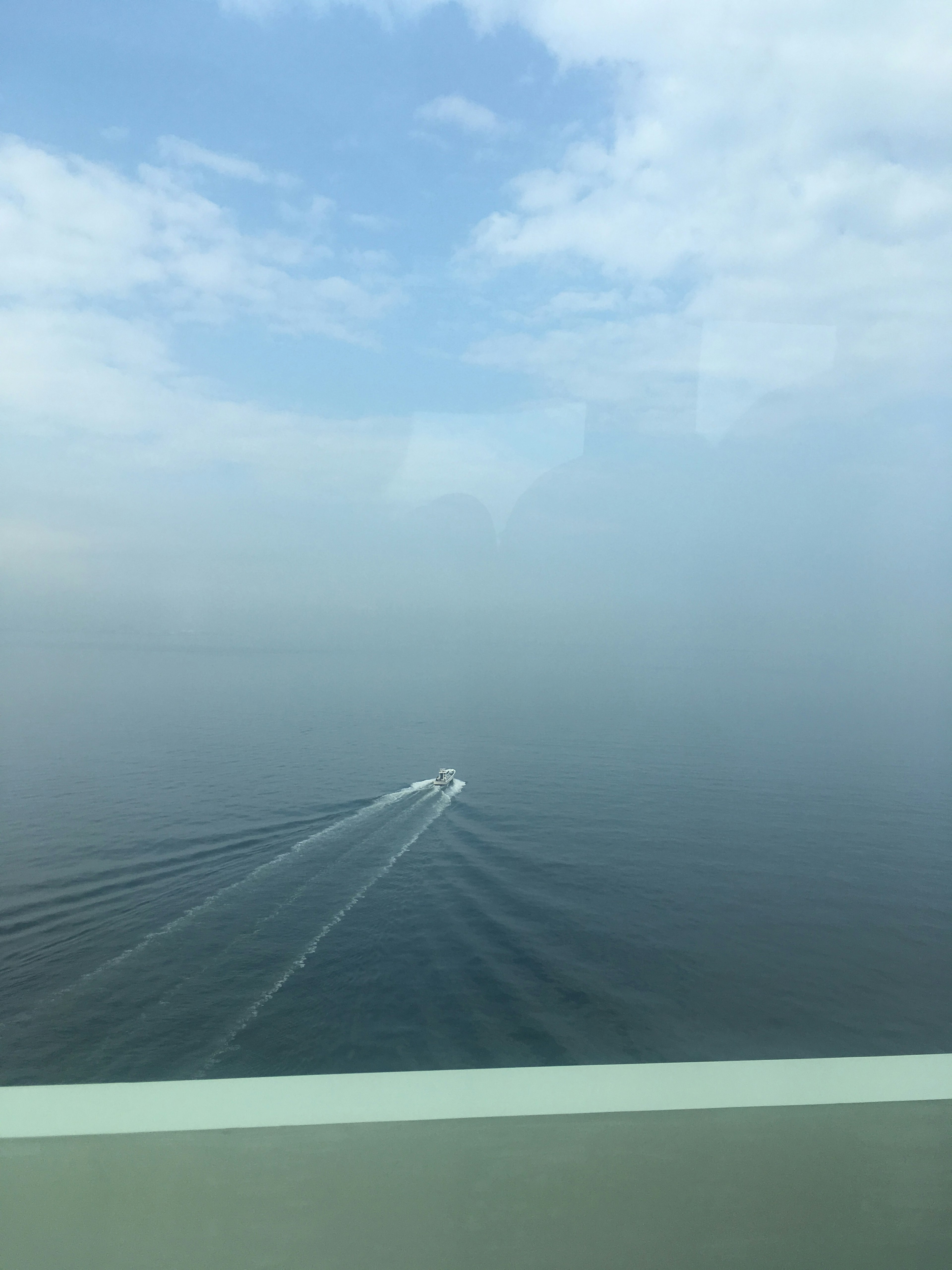 Small boat navigating through fog with calm sea backdrop