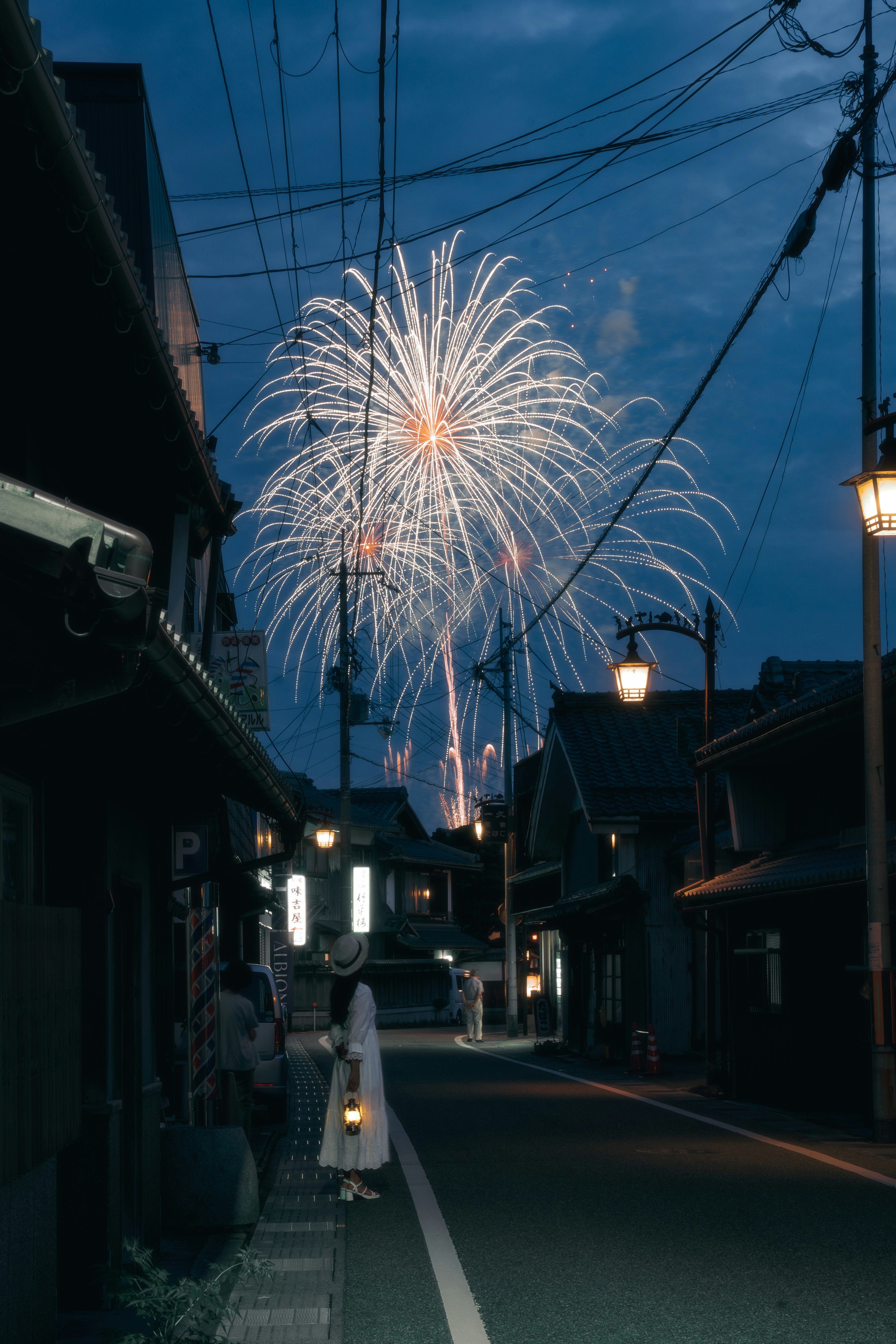 Une scène de rue avec des feux d'artifice dans le ciel nocturne et une personne vêtue de blanc