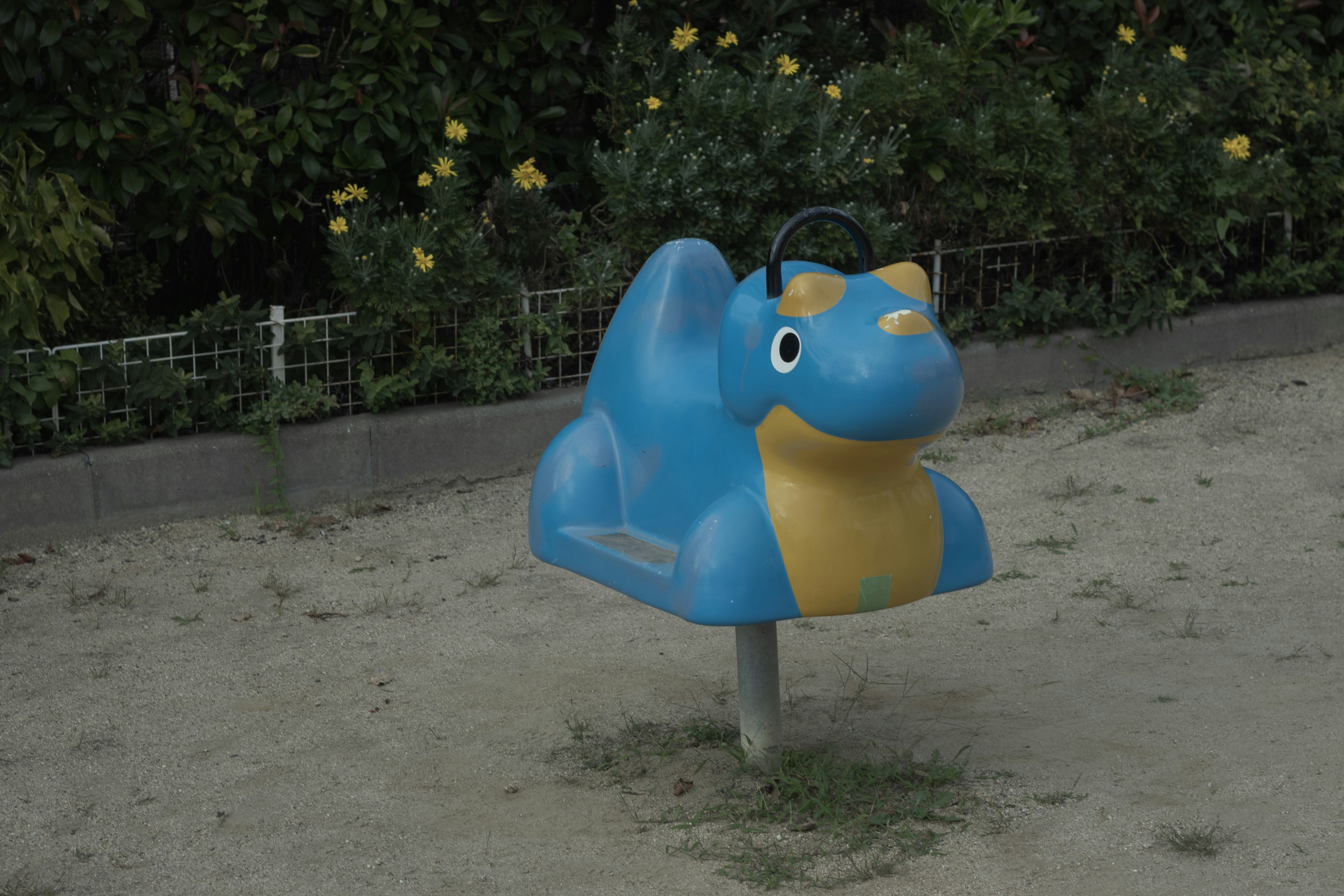 Blue dinosaur-shaped playground equipment in a sandy area