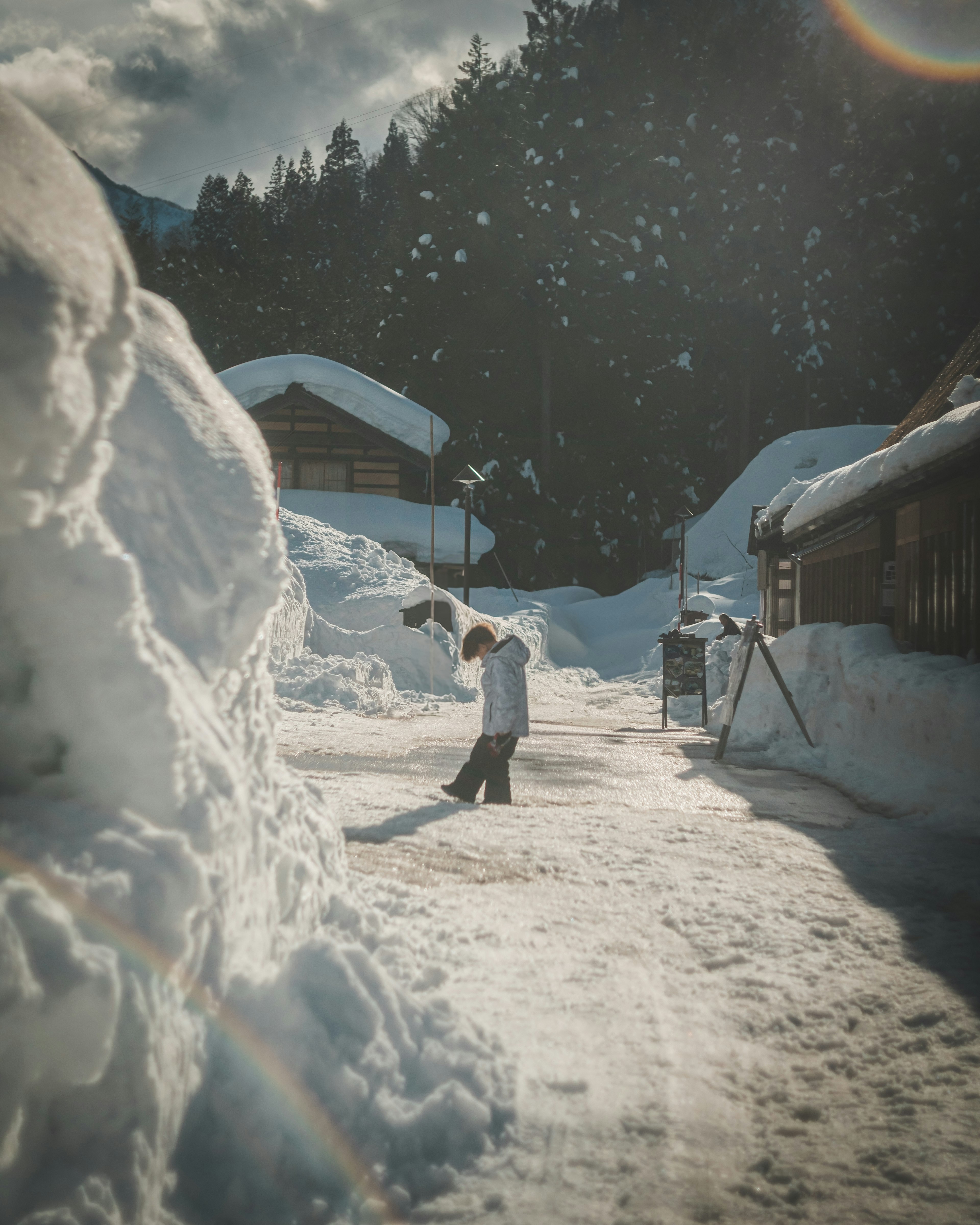 Person geht auf einem schneebedeckten Weg in einem Dorf mit Schneehaufen