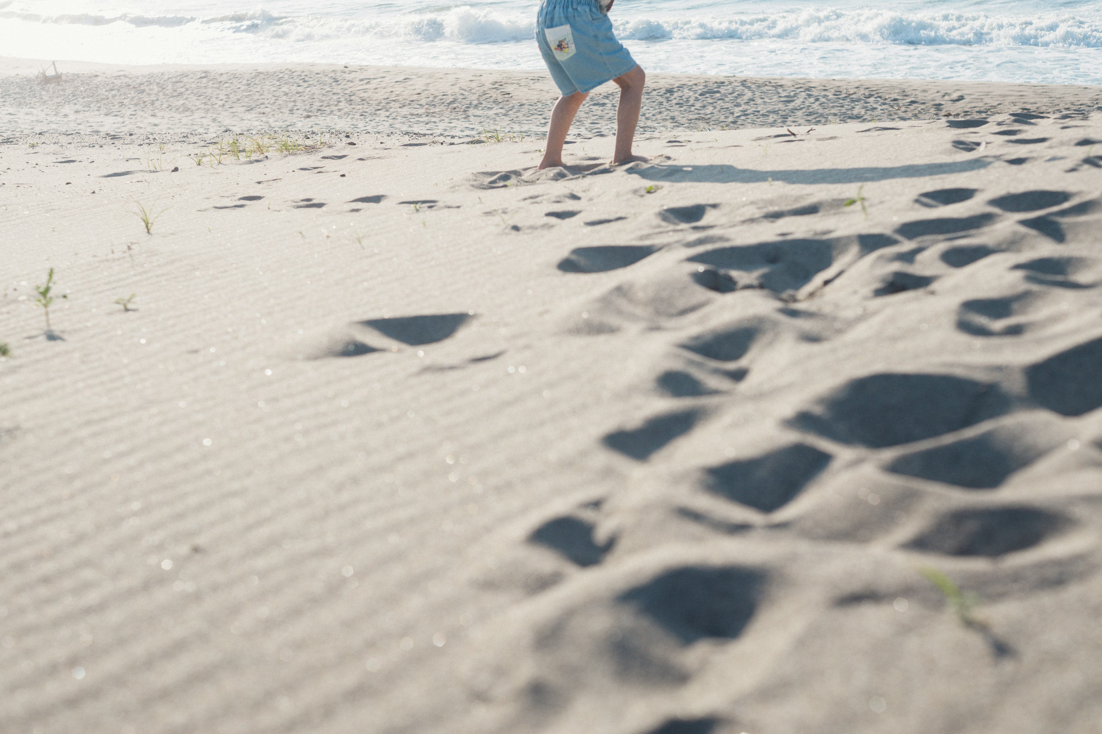 A person walking on the beach leaving footprints with ocean waves in the background