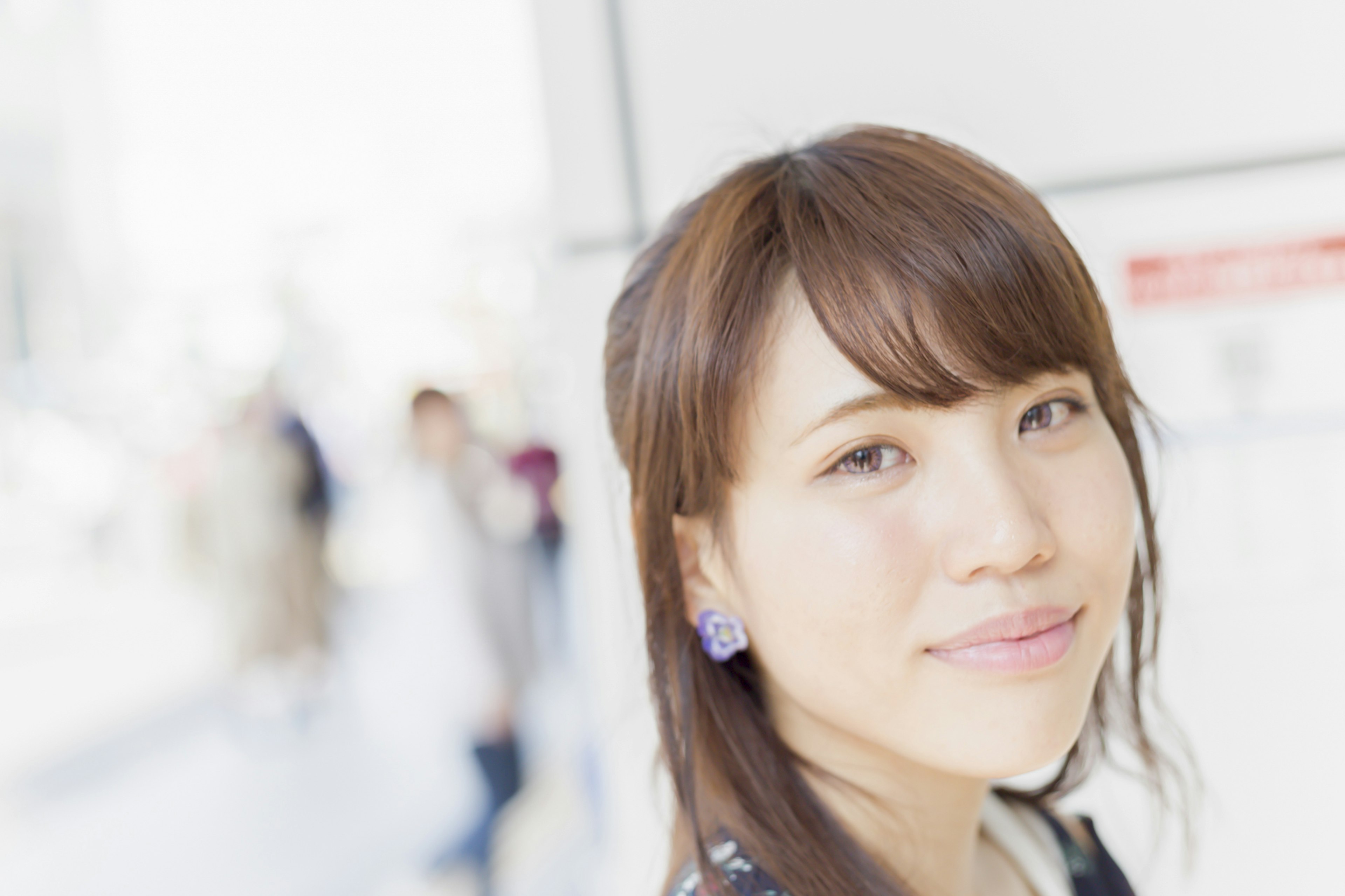 A smiling woman with brown hair and earrings in a bright background