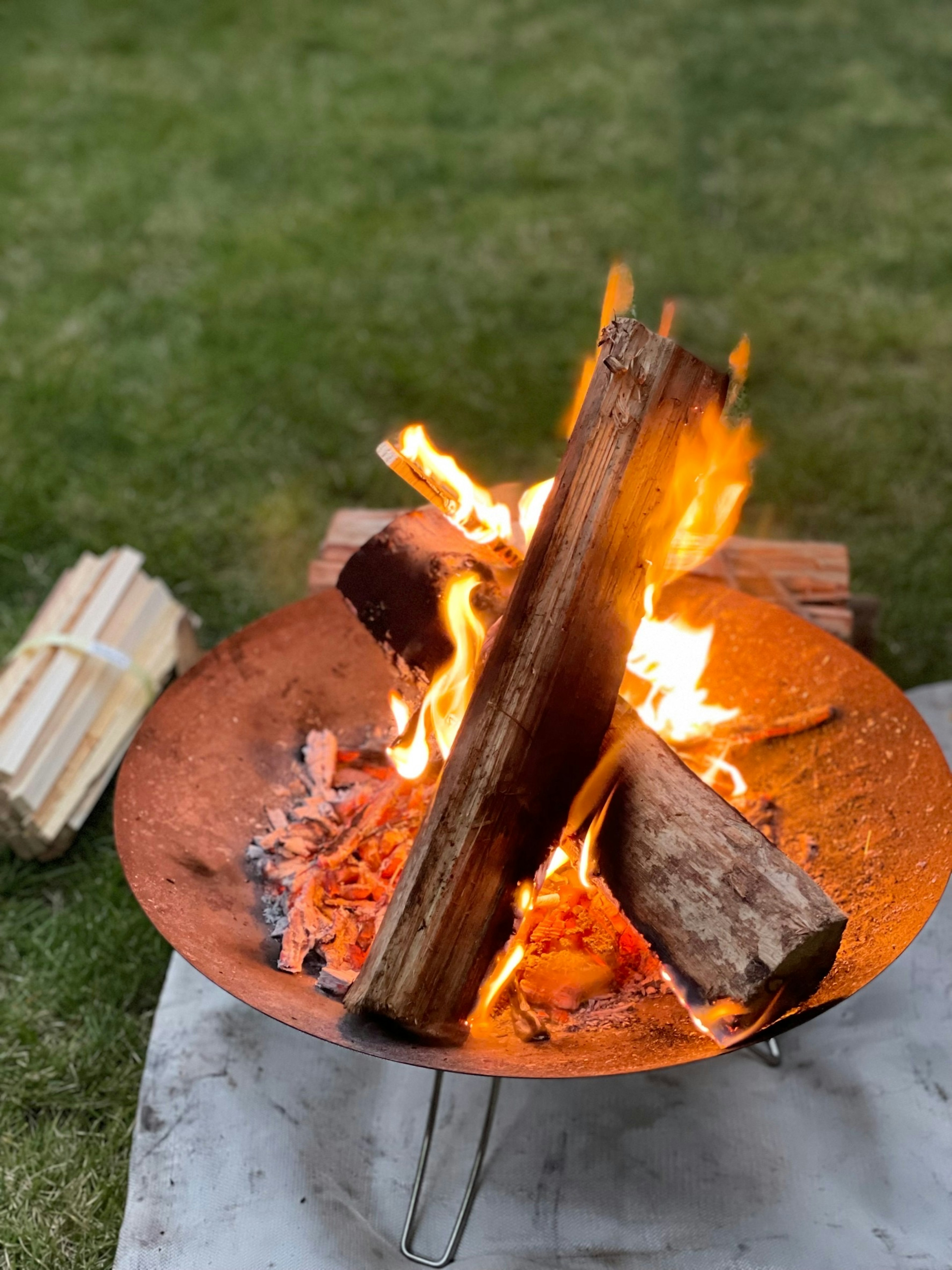 A fire burning in a fire pit with logs and grass surrounding