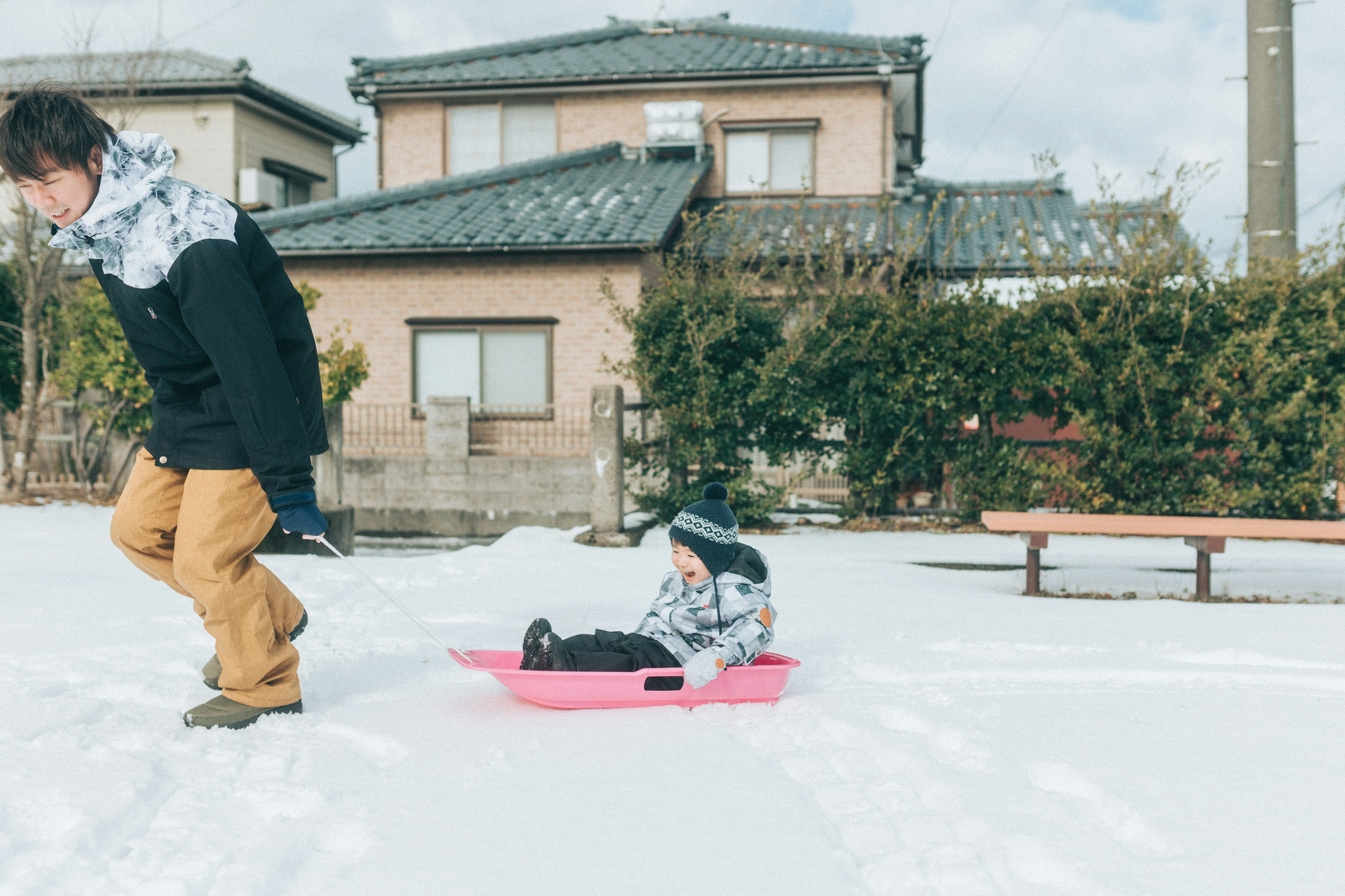 Un bambino che si diverte a slittare nella neve con un adulto che corre davanti