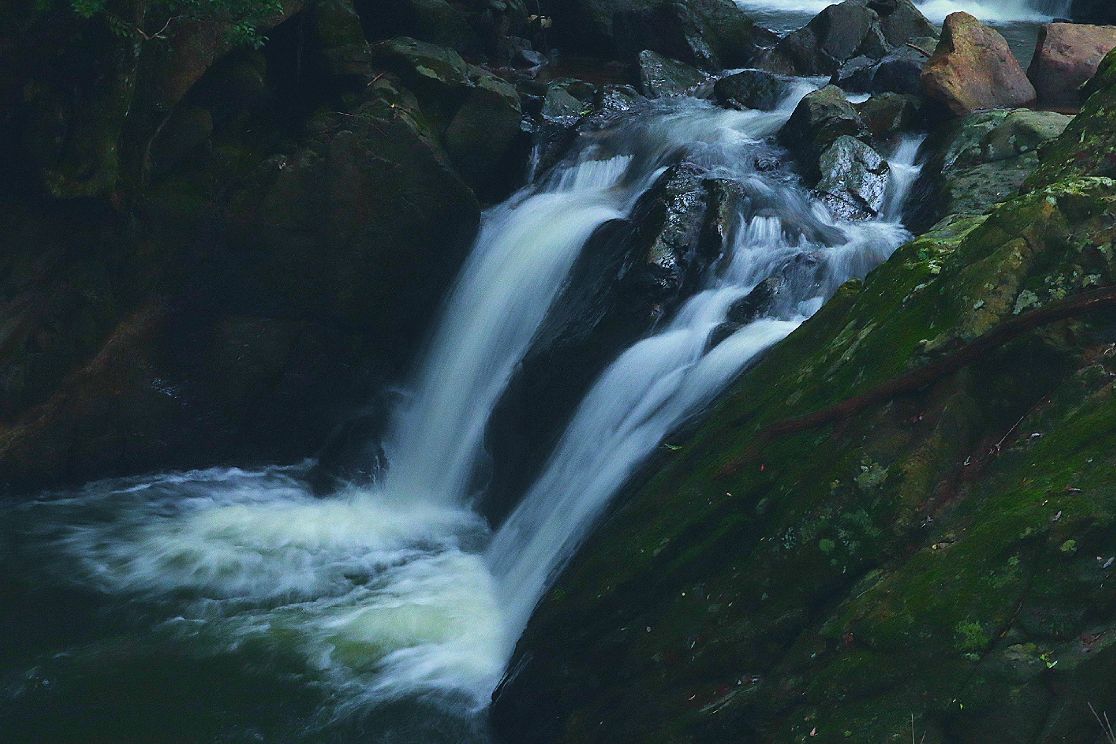 Wasserfall, der über moosbedeckte Felsen fließt, umgeben von Grün