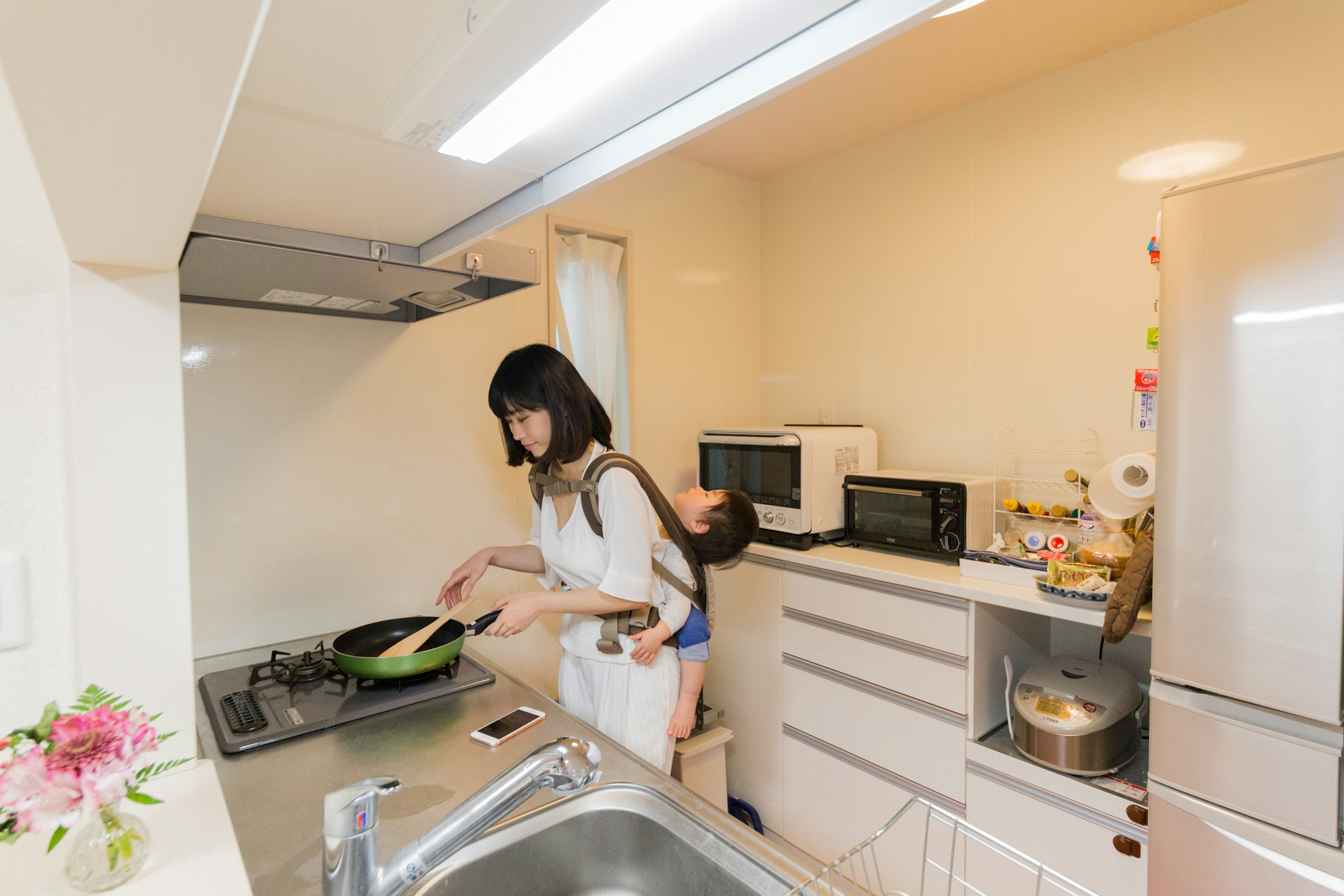 Cuisine lumineuse avec une femme cuisinant et un enfant sur son dos