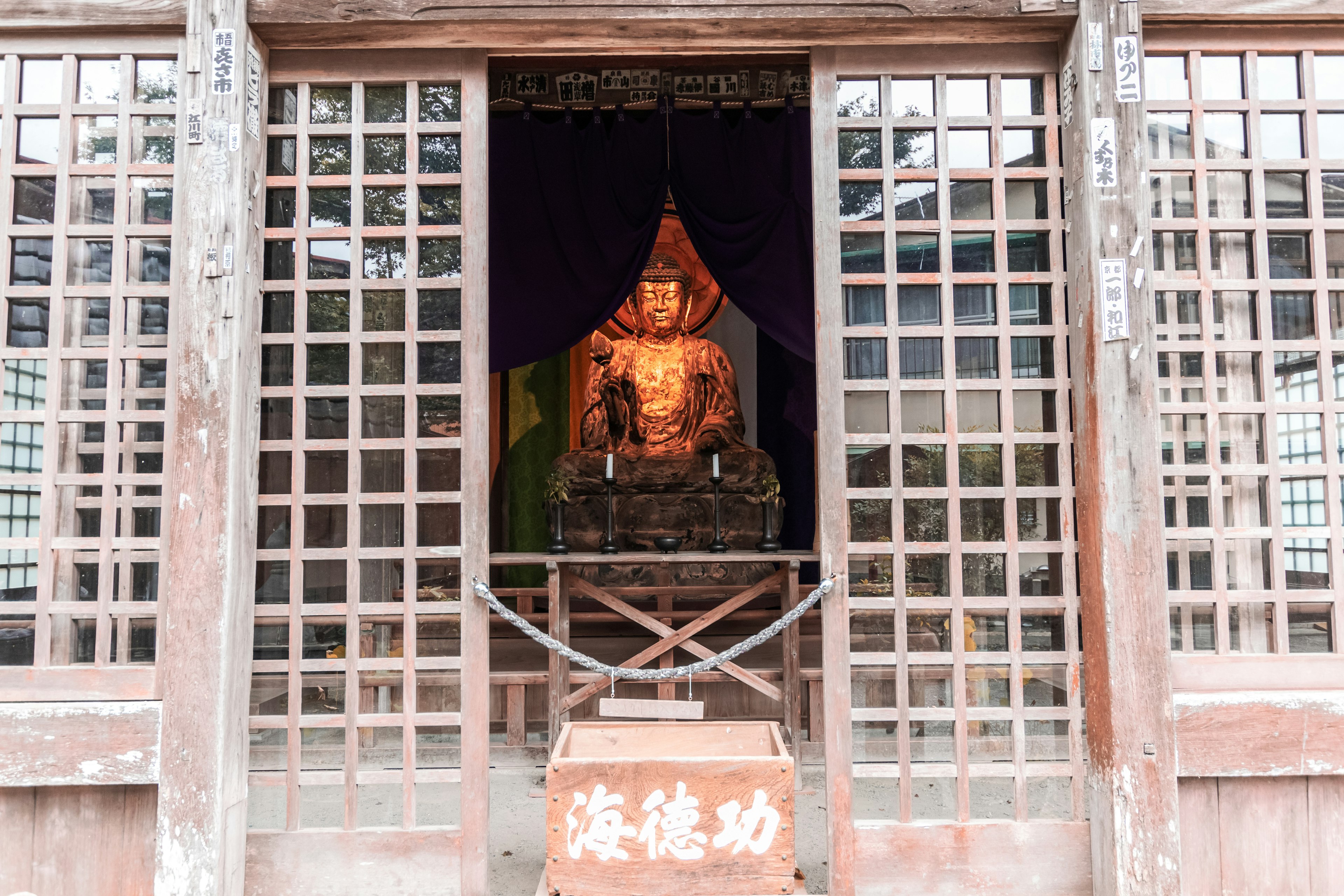 Finestra a graticcio in legno che rivela una statua del Buddha e l'interno del santuario