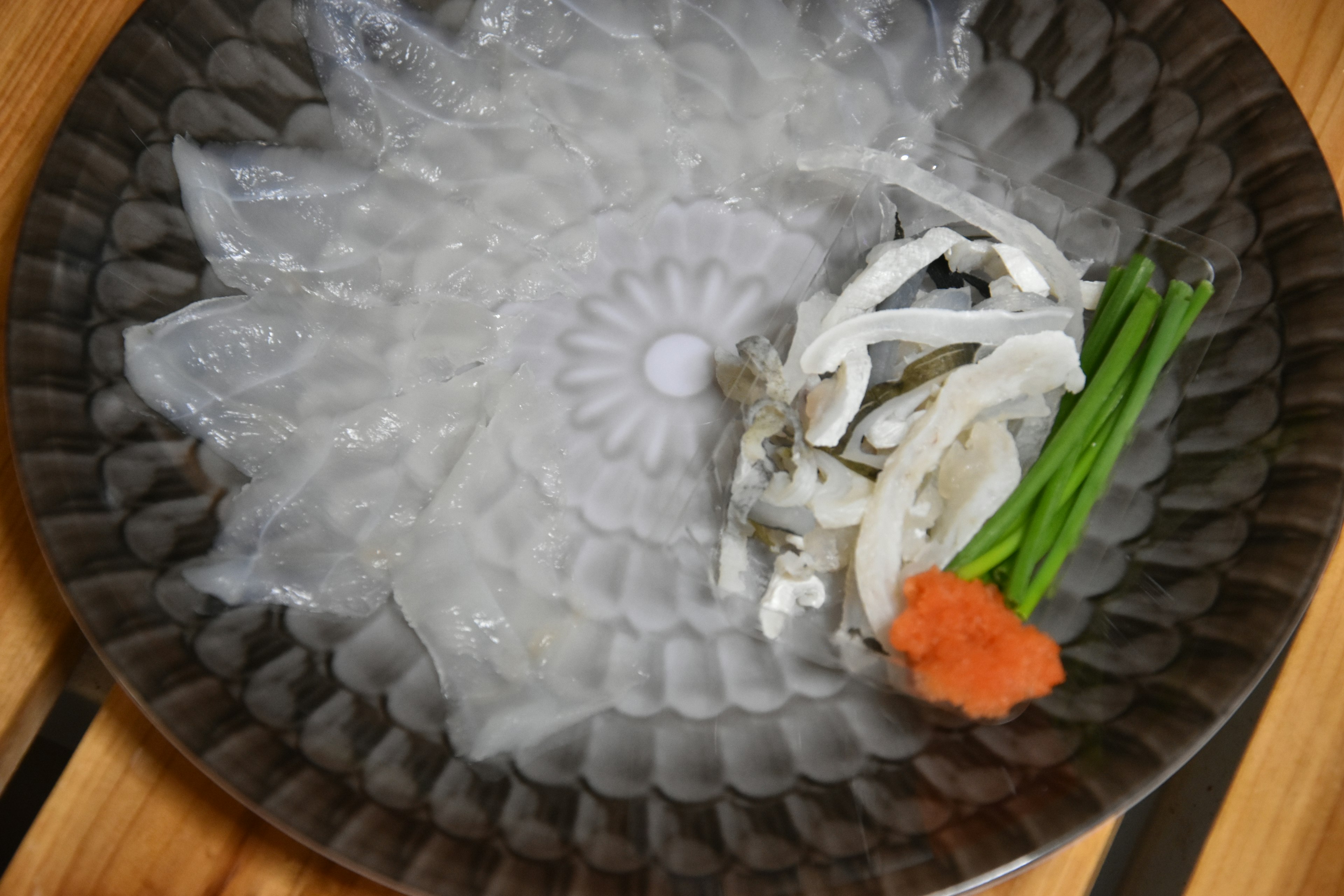 A plate with translucent sashimi and garnishes including green onions and orange paste