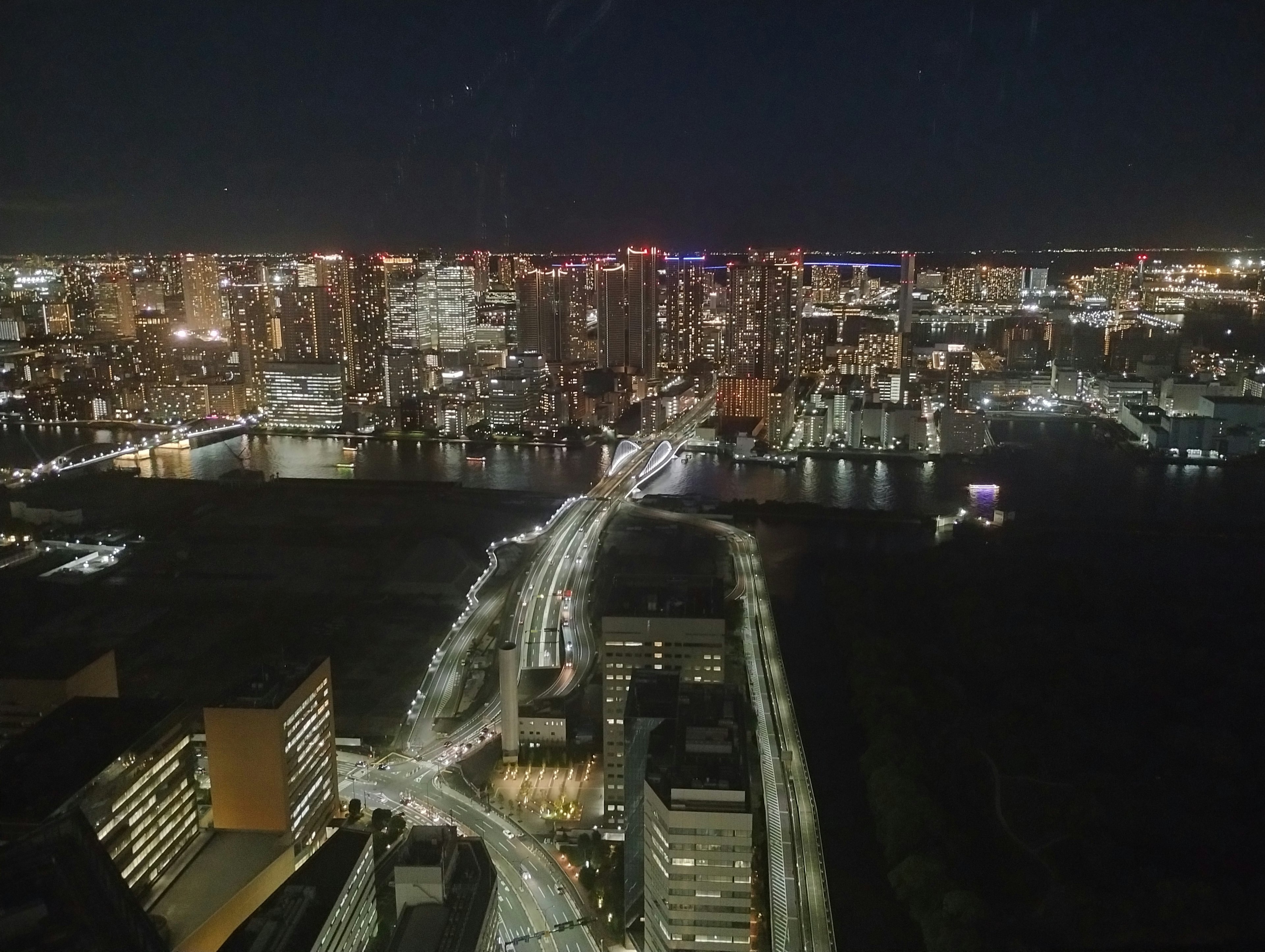 Night view of a city skyline featuring tall buildings and a river