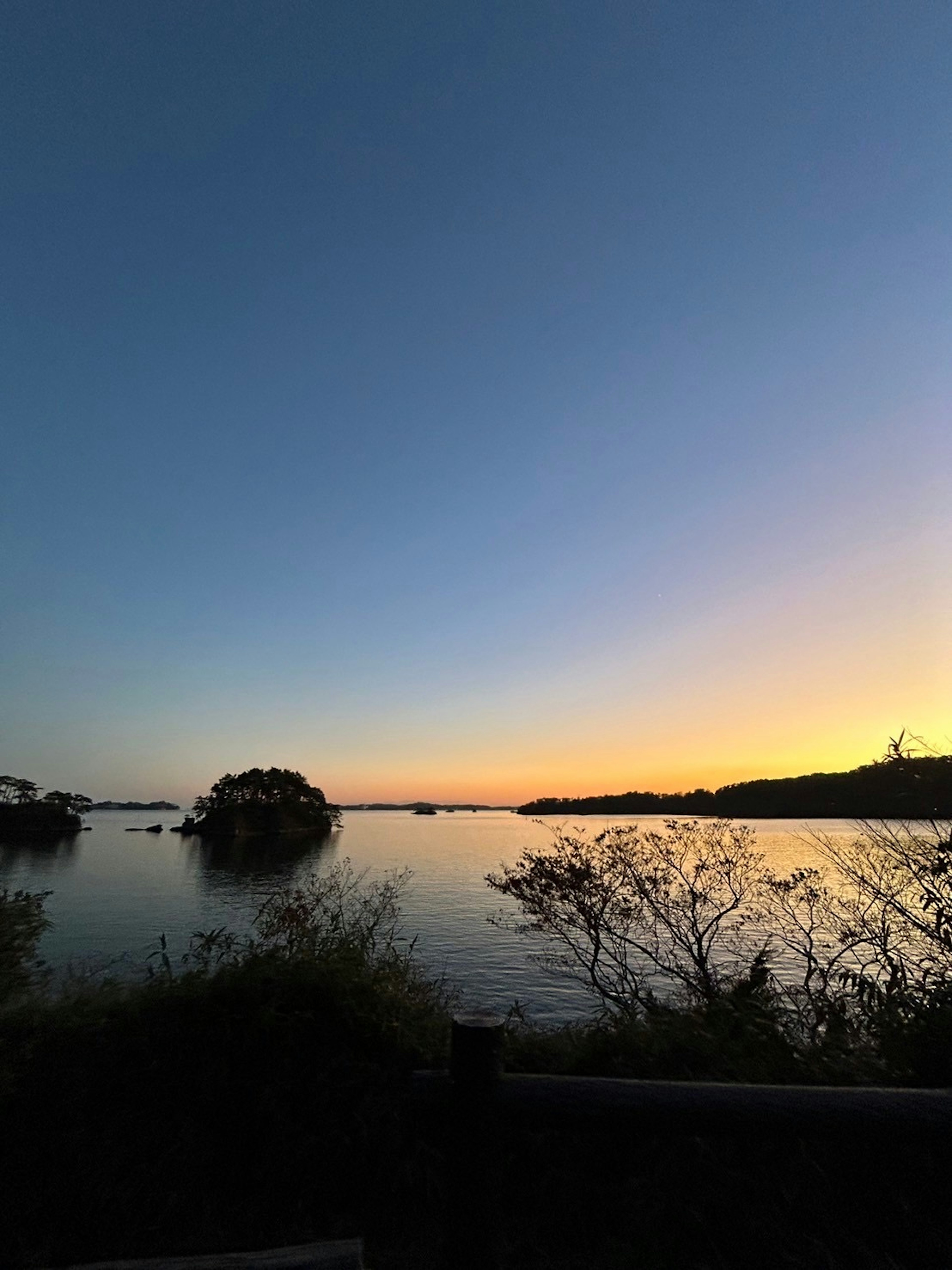 夕暮れの湖の風景、静かな水面、遠くの島々、青からオレンジのグラデーション