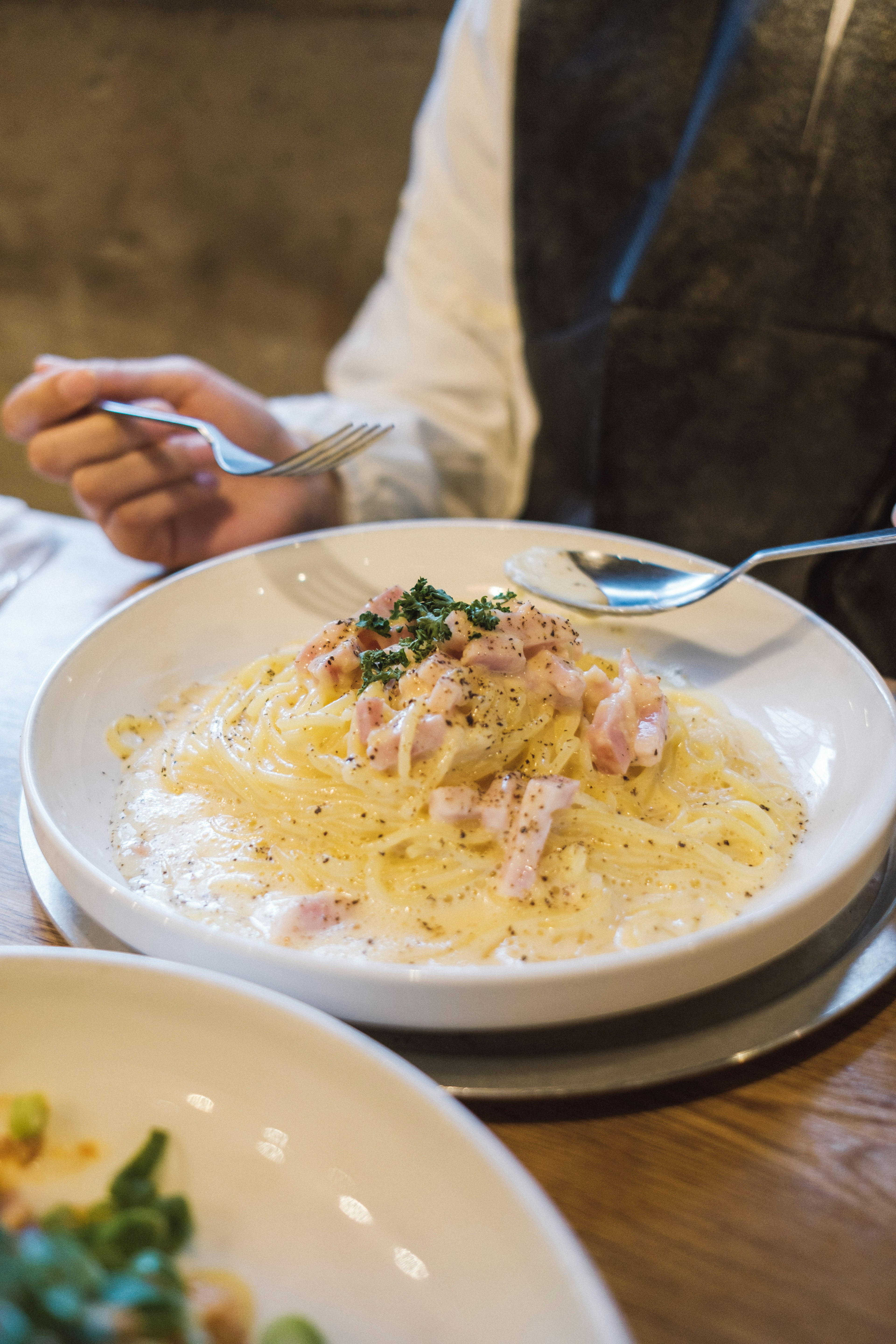 Cream sauce pasta on a white plate with a hand holding a fork