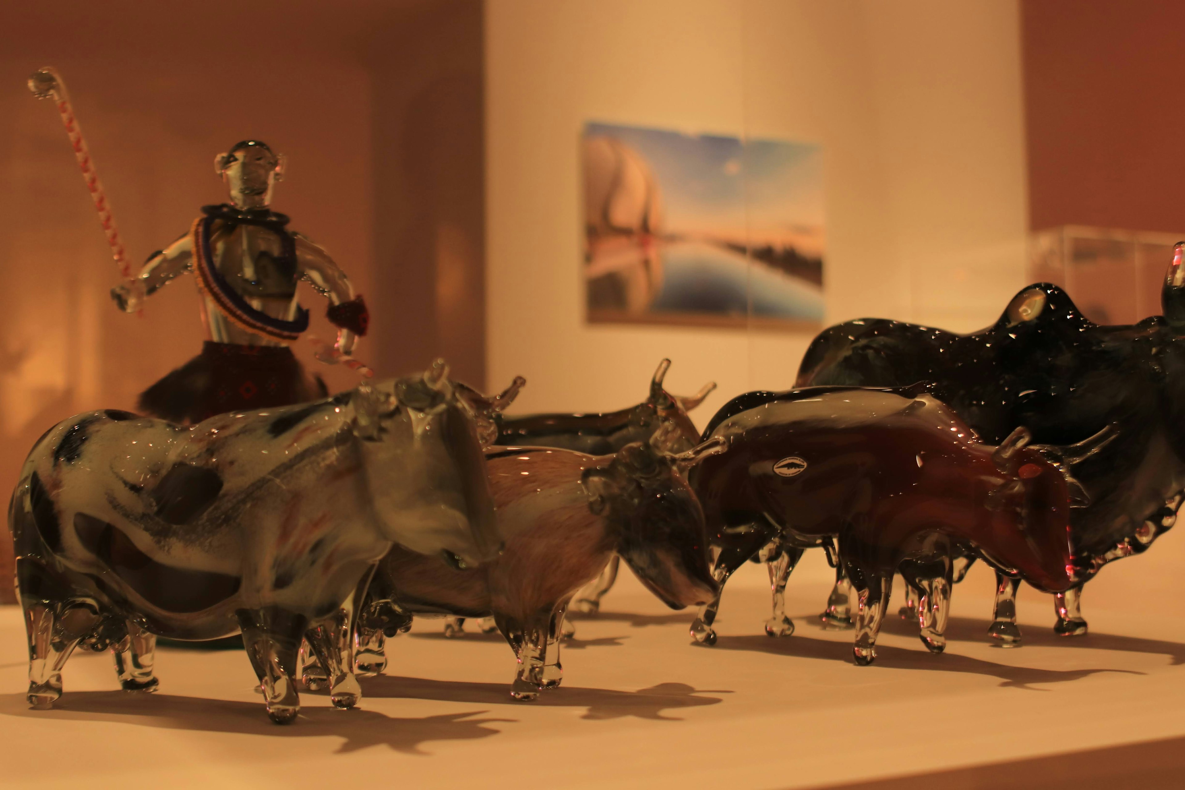 A display of glass sculptures of cows with a warrior figure in the foreground