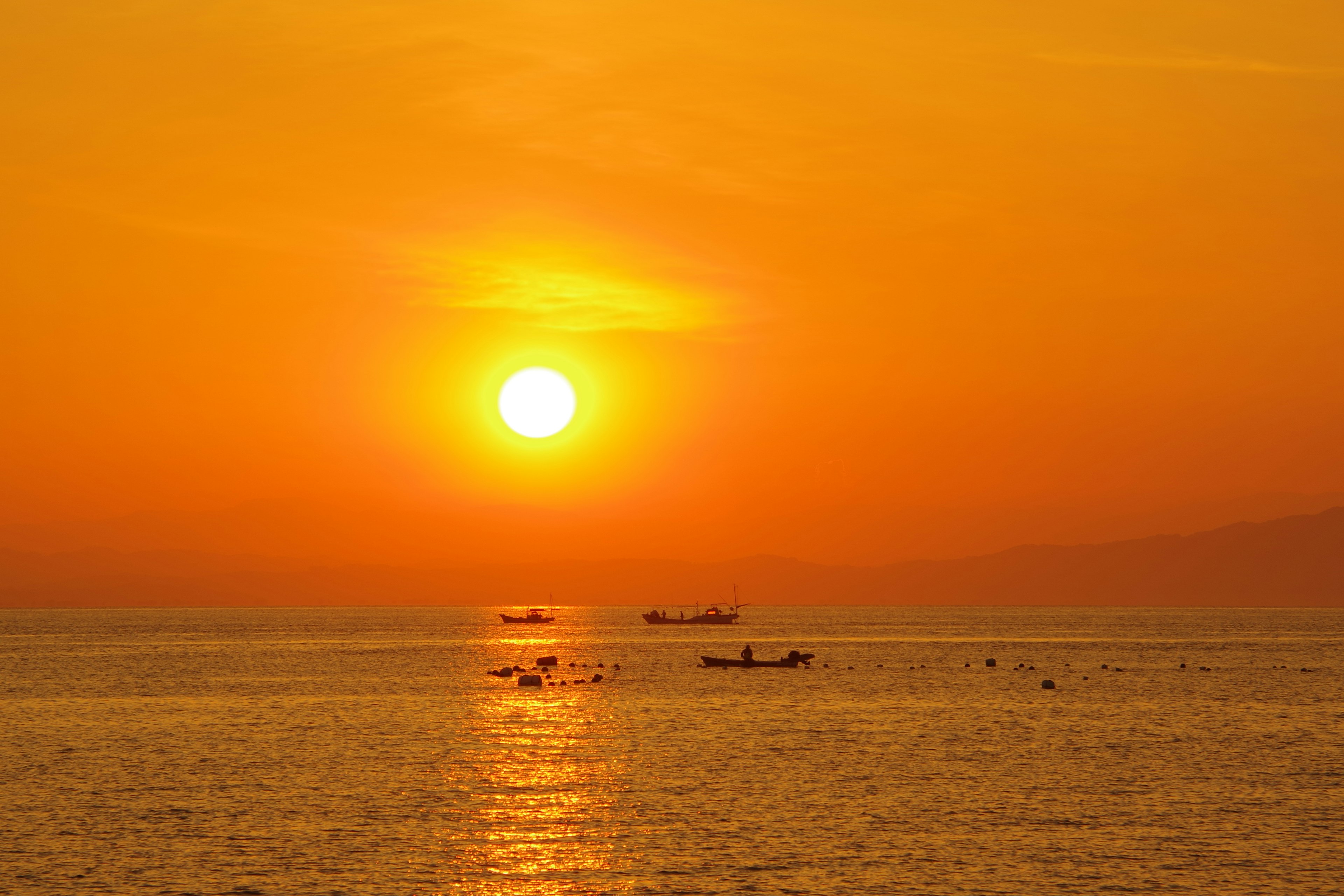 Schöner orangefarbener Sonnenuntergang über dem Meer mit Booten in der Ferne