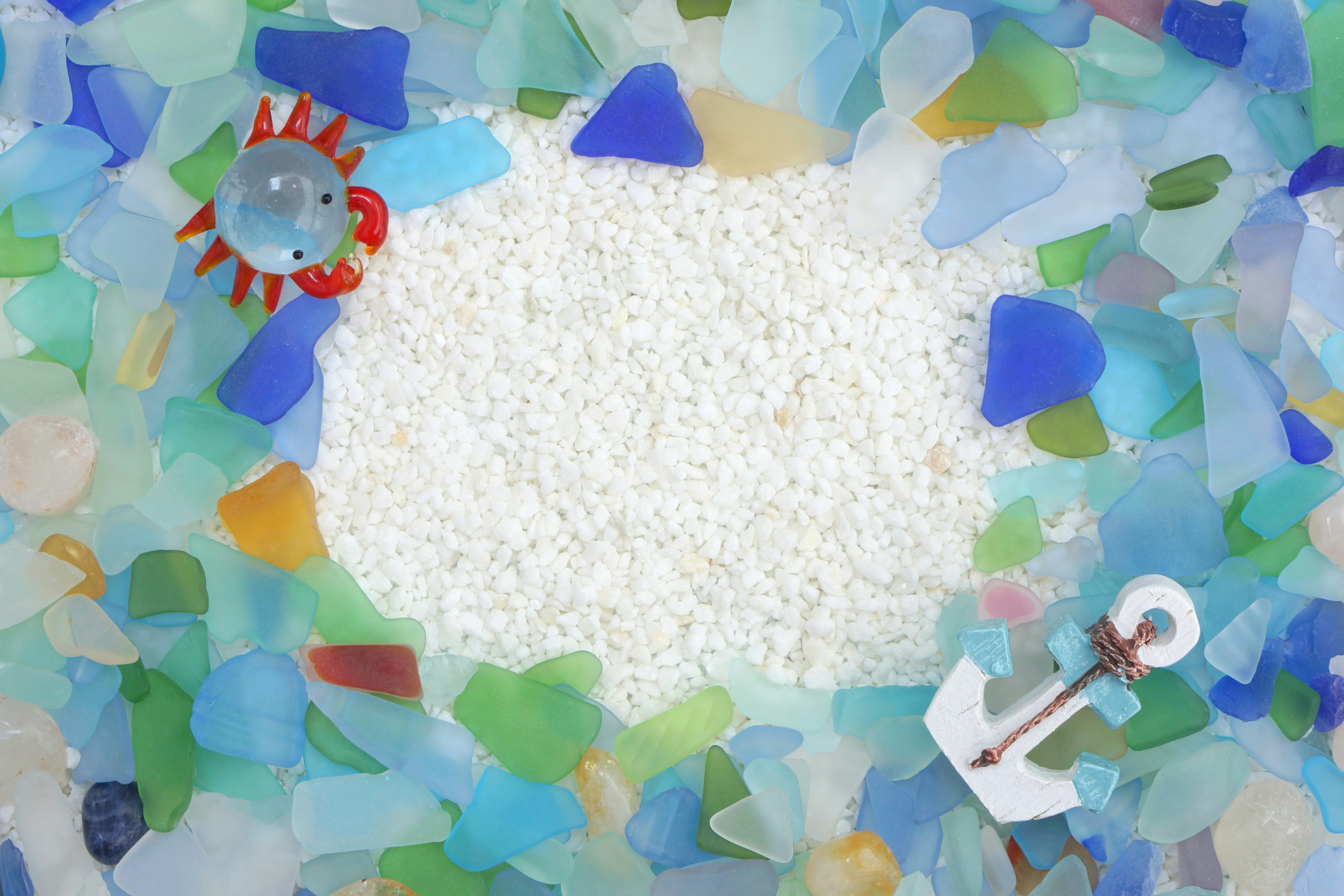 Colorful glass fragments surround a white sand area featuring a red crab and a white anchor