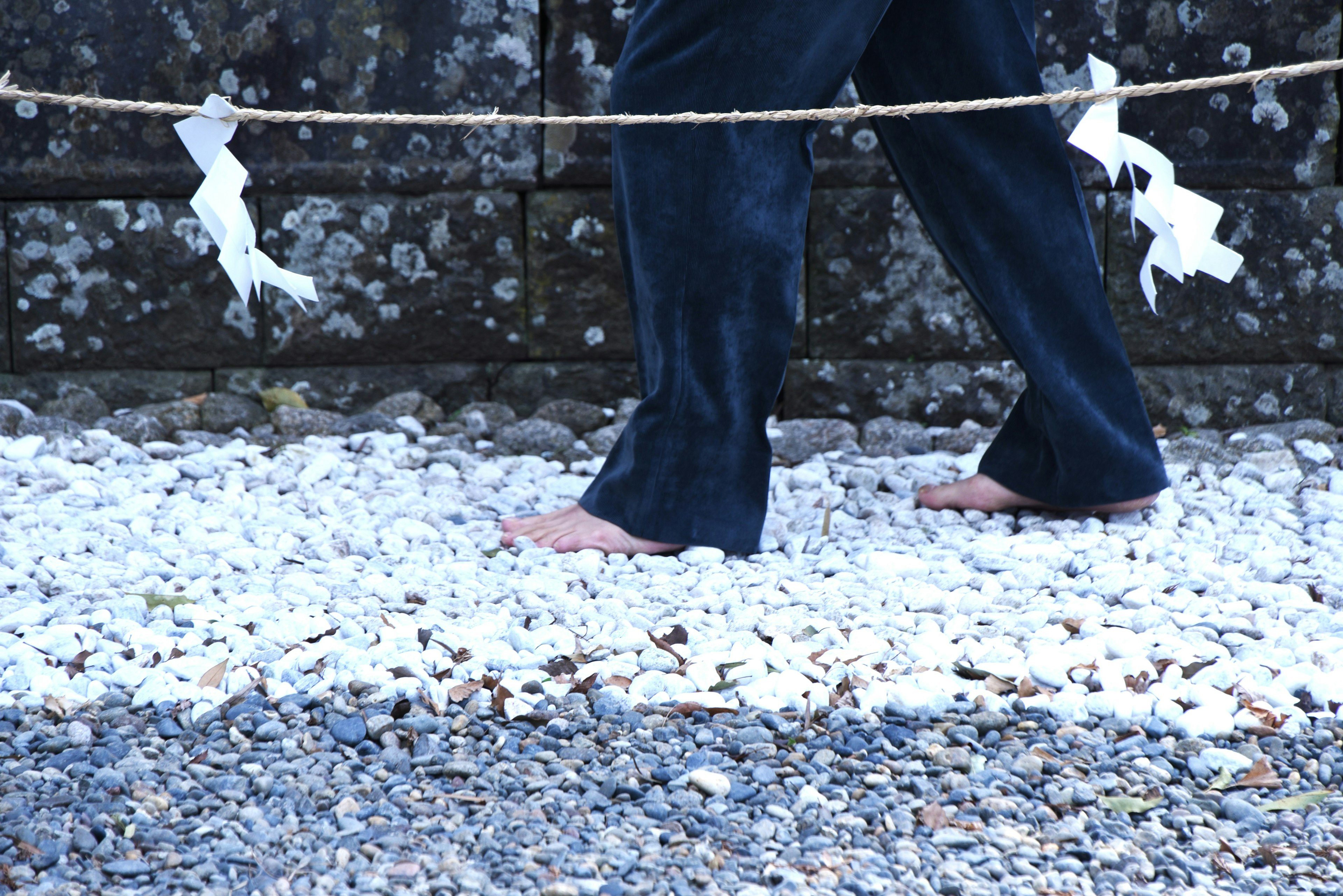 A person walking barefoot on white gravel with a stone wall in the background