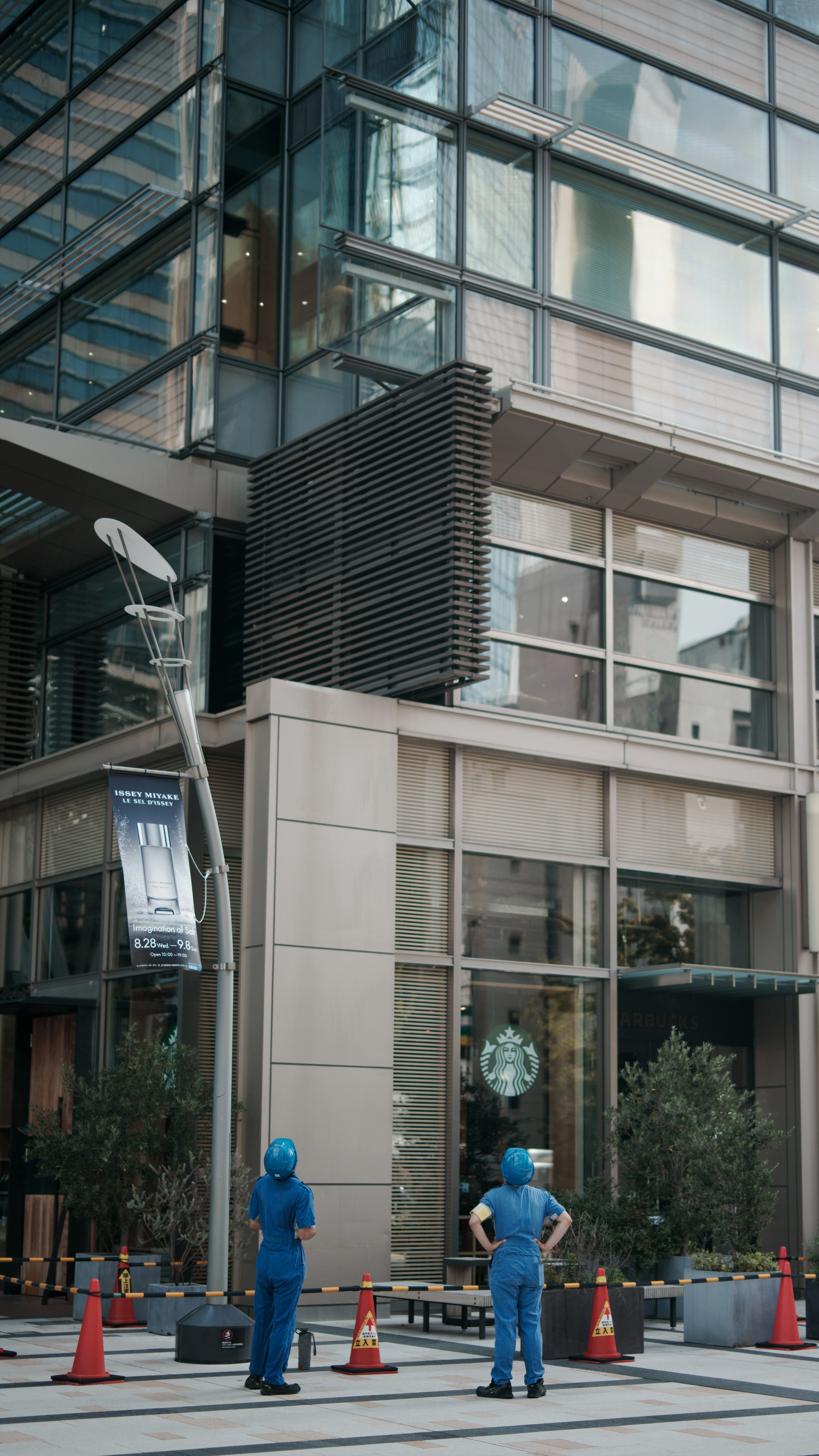 Dua pekerja berpakaian biru berdiri di depan Starbucks di sebuah bangunan modern