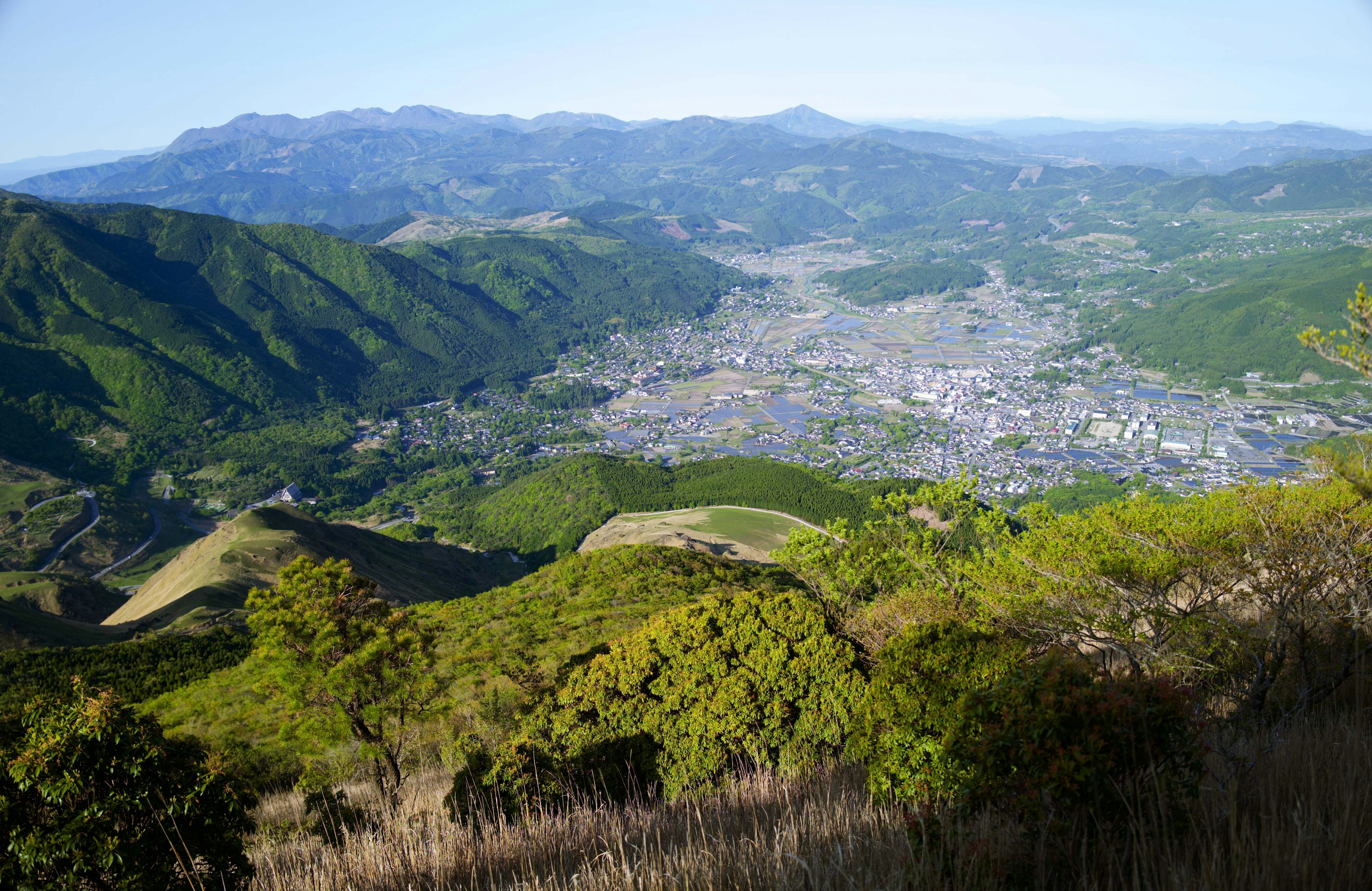 Vue panoramique d'une ville entourée de montagnes végétation luxuriante et ciel bleu clair