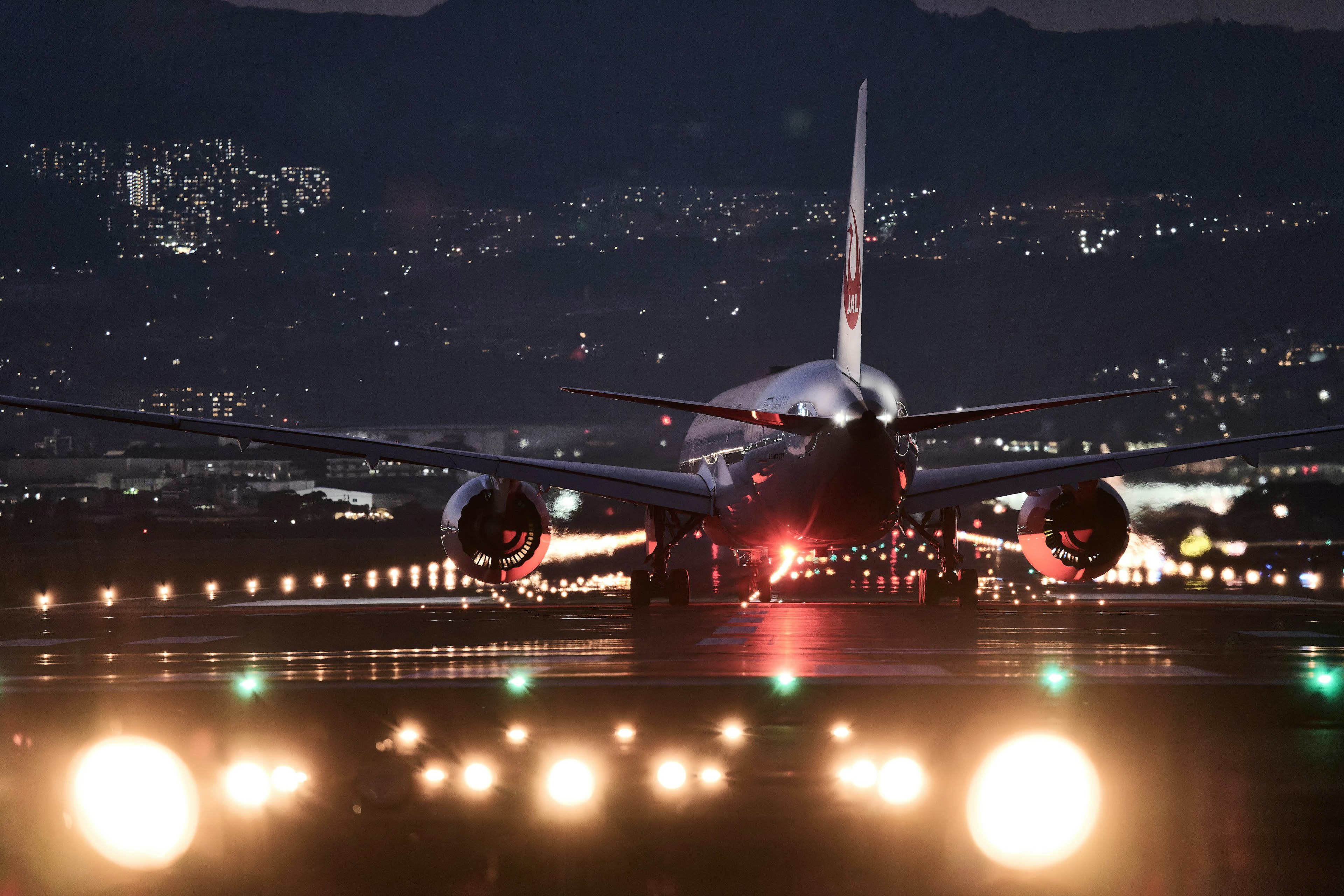 夜の滑走路に立つ航空機の後ろ姿と明るい滑走路灯