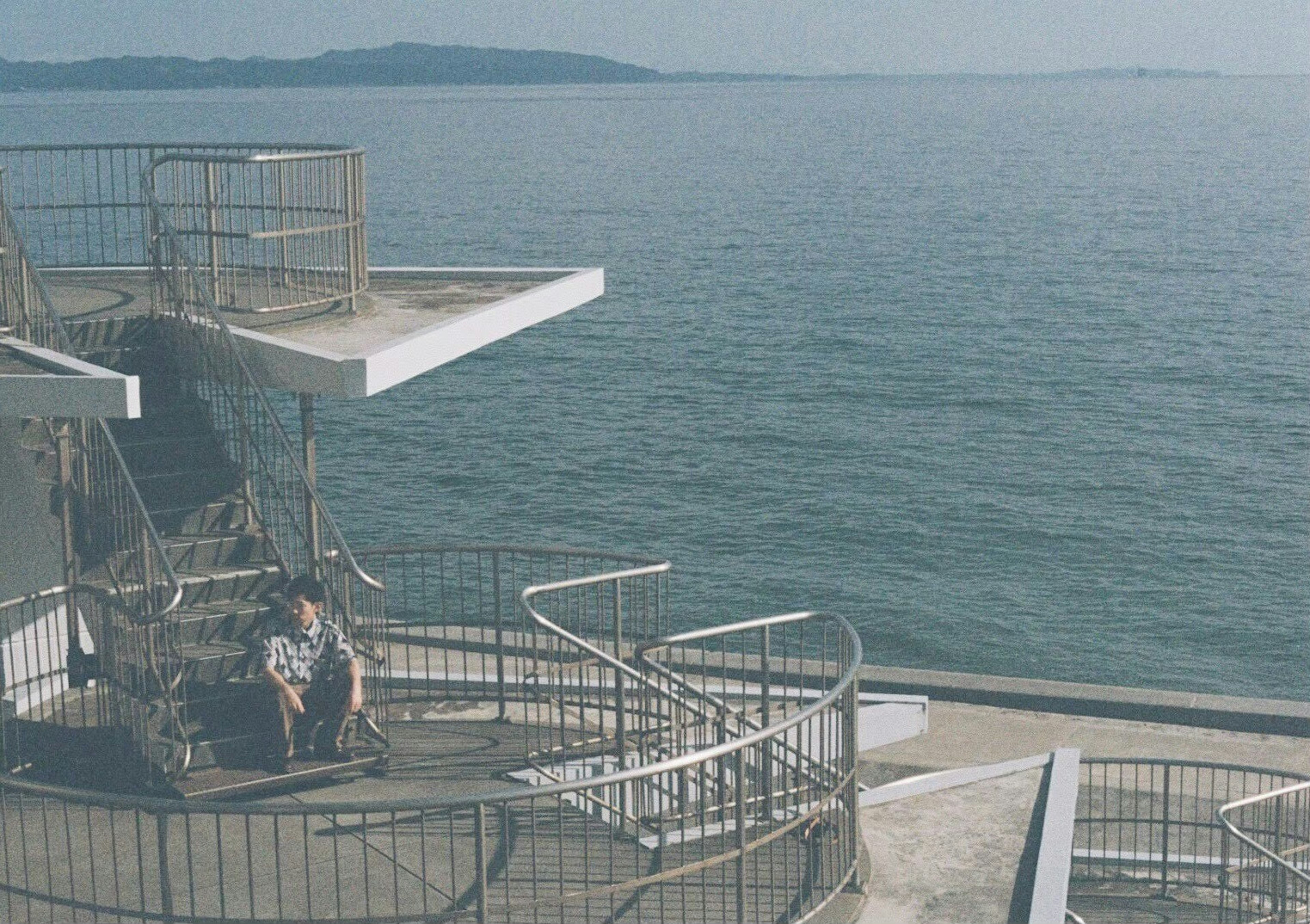 Person sitting on a staircase and platform near the sea