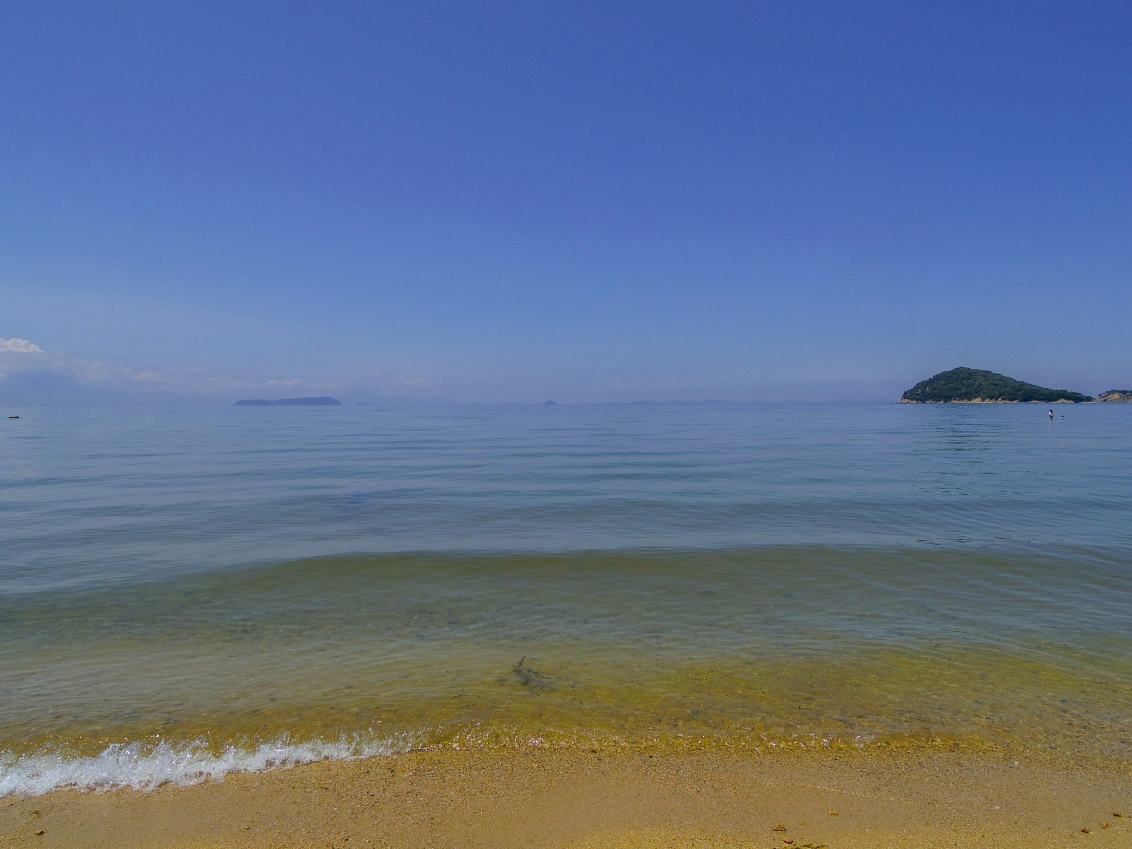 Mer calme avec ciel bleu et île lointaine surface d'eau claire et plage de sable