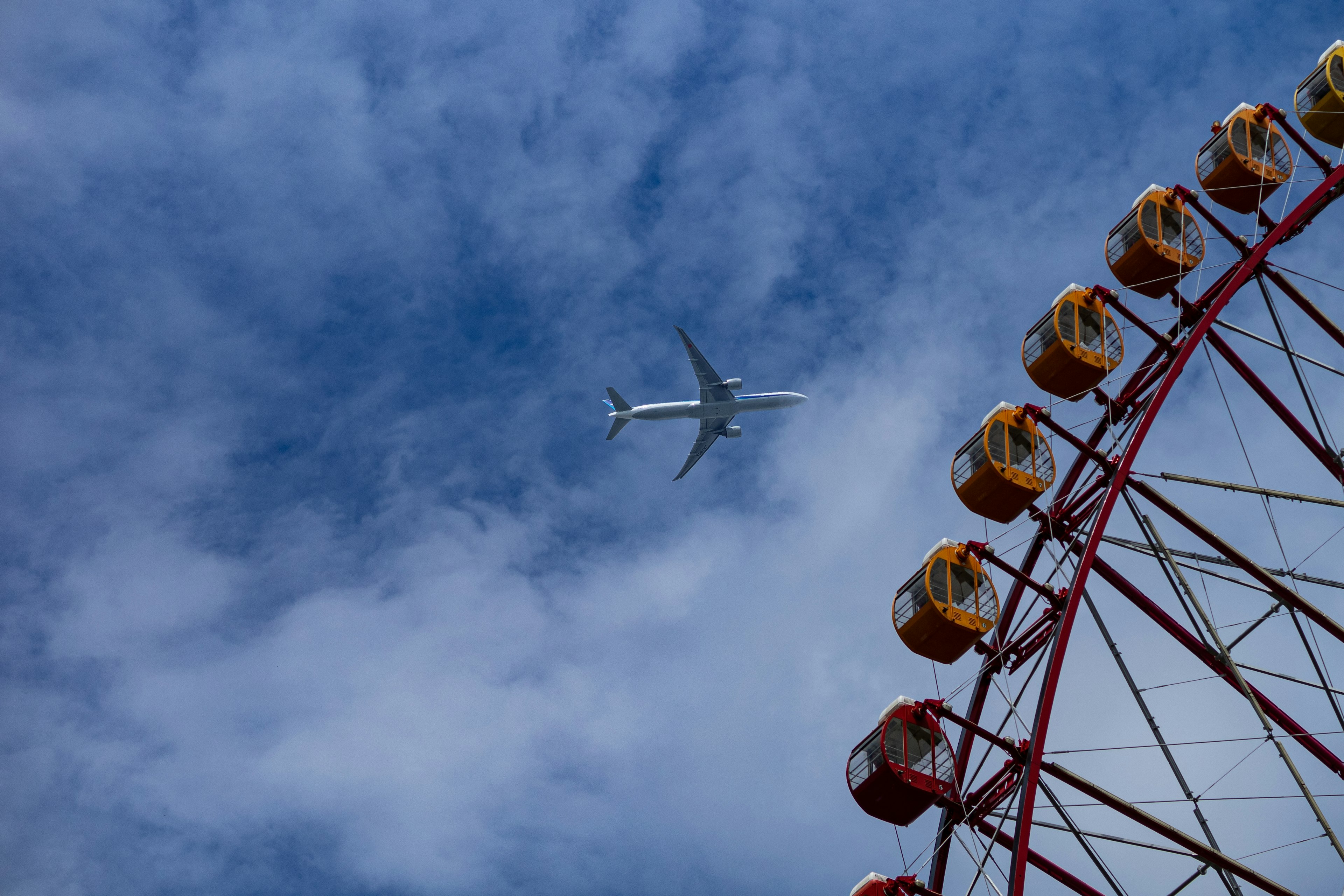 青空の下に観覧車と飛行機が飛んでいるシーン