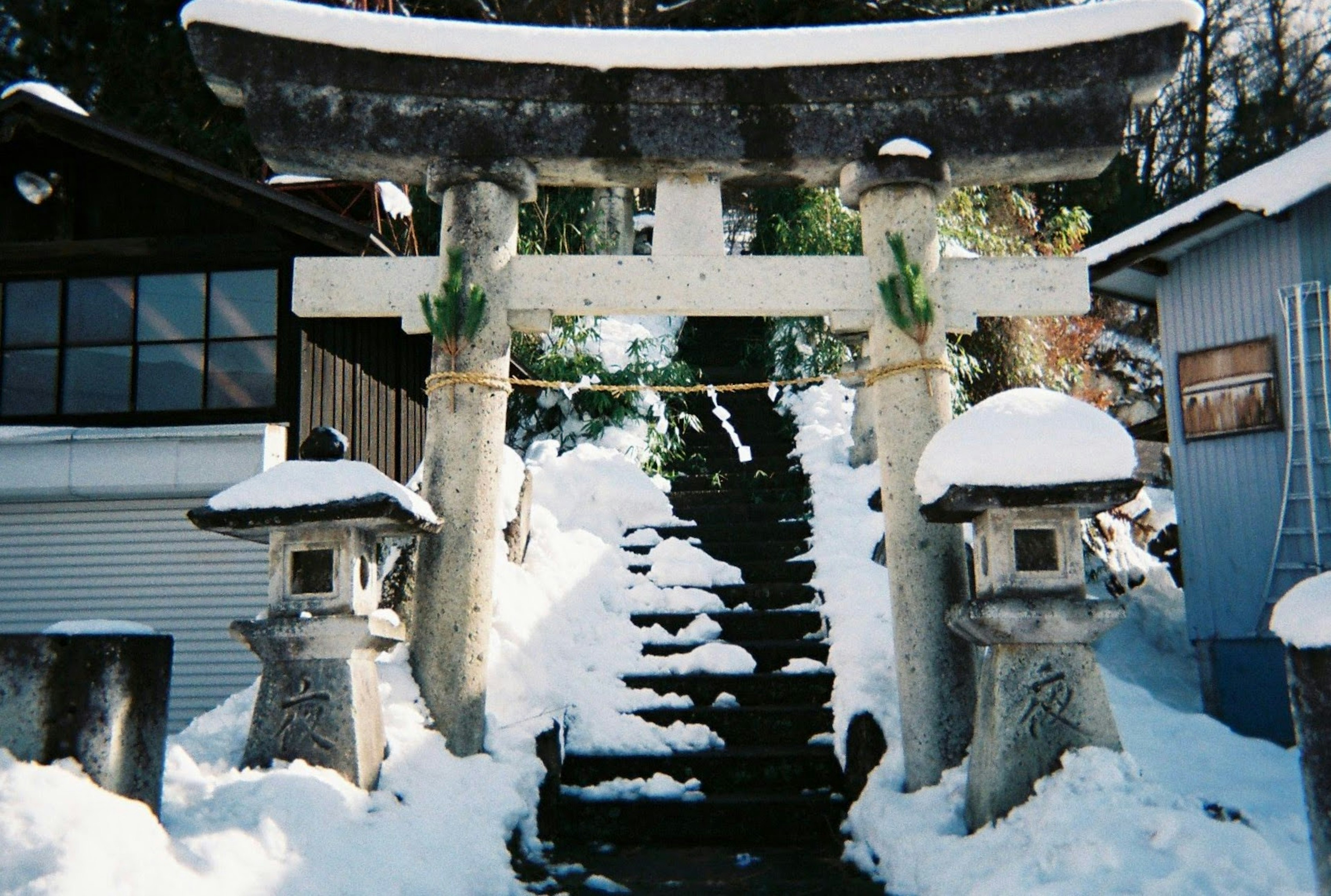 Portail torii enneigé et lanternes en pierre à côté des escaliers