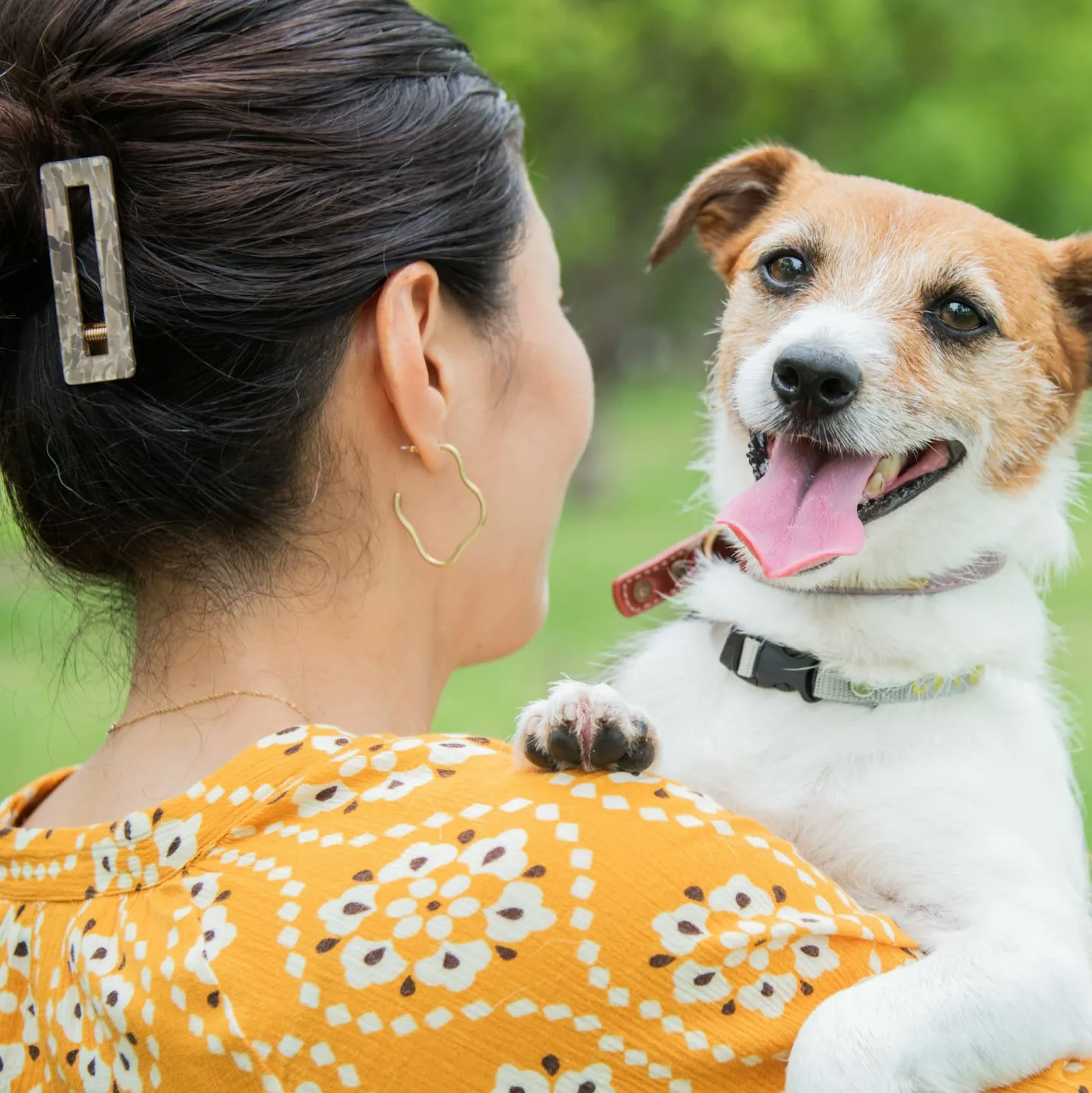 Femme tenant un chien avec une expression joyeuse dans un cadre extérieur verdoyant