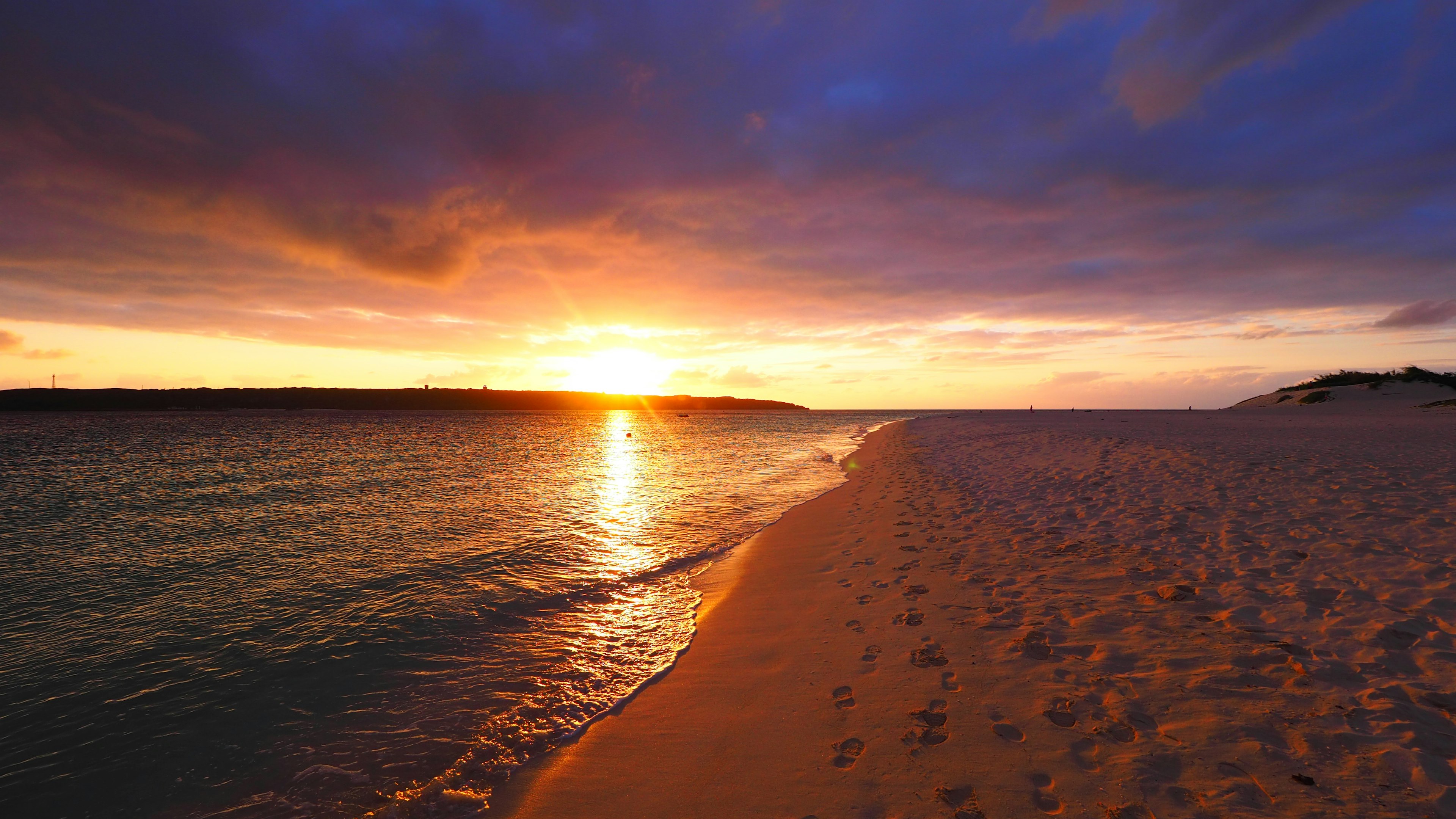 วิวชายหาดที่สวยงามในยามพระอาทิตย์ตกพร้อมทรายและคลื่นเบา