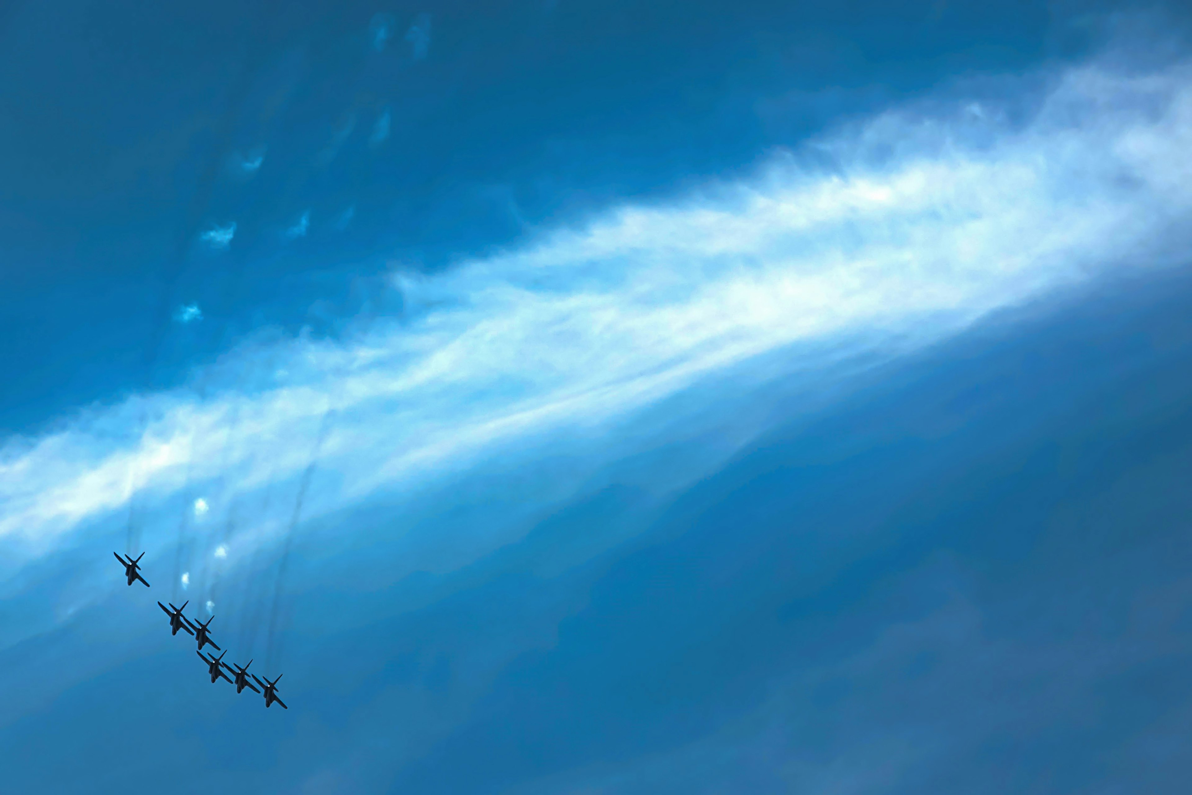 A formation of aircraft flying in the blue sky with a white cloud trail