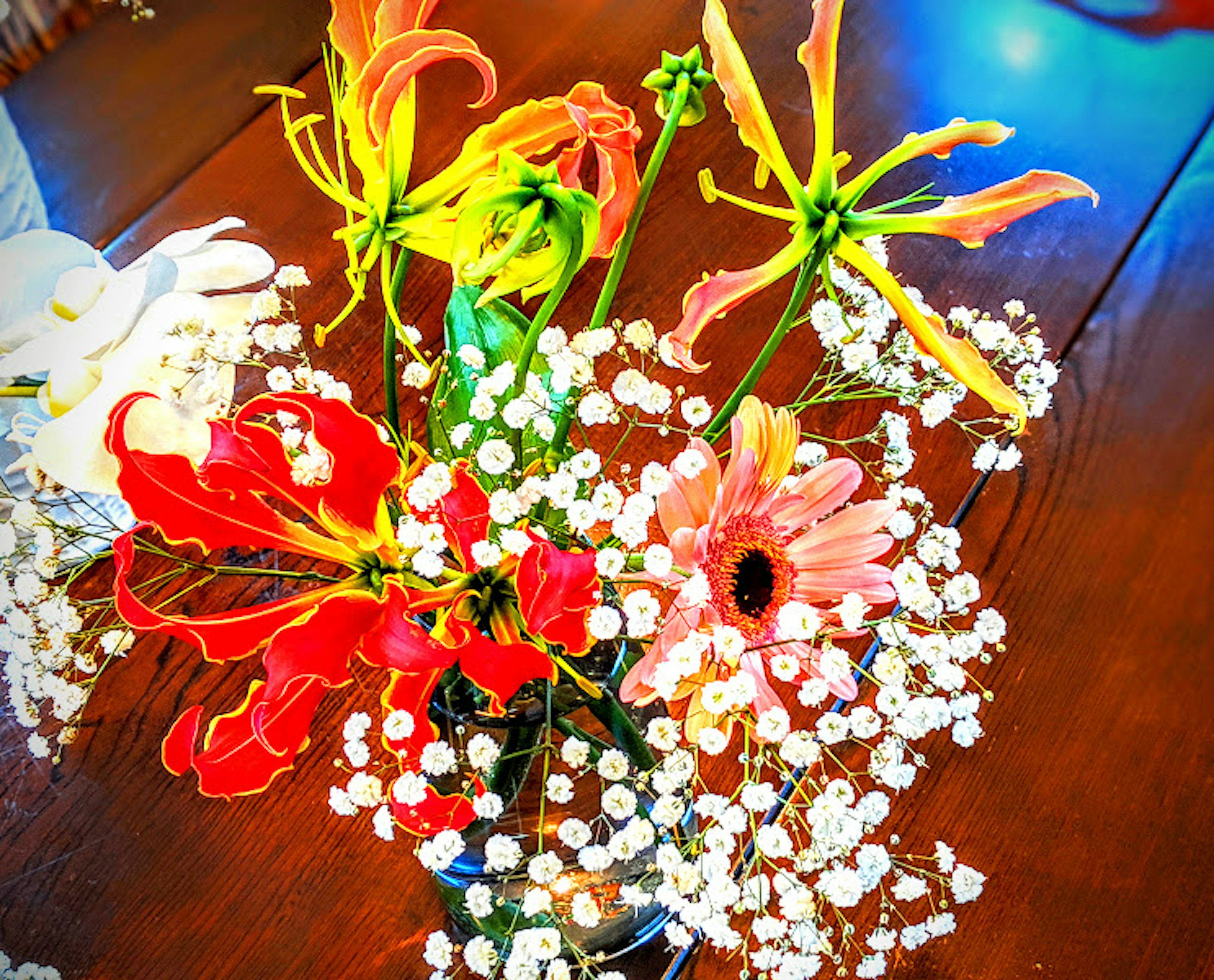 A vibrant bouquet featuring red gloriosa lilies and assorted colorful flowers surrounded by white baby’s breath flowers