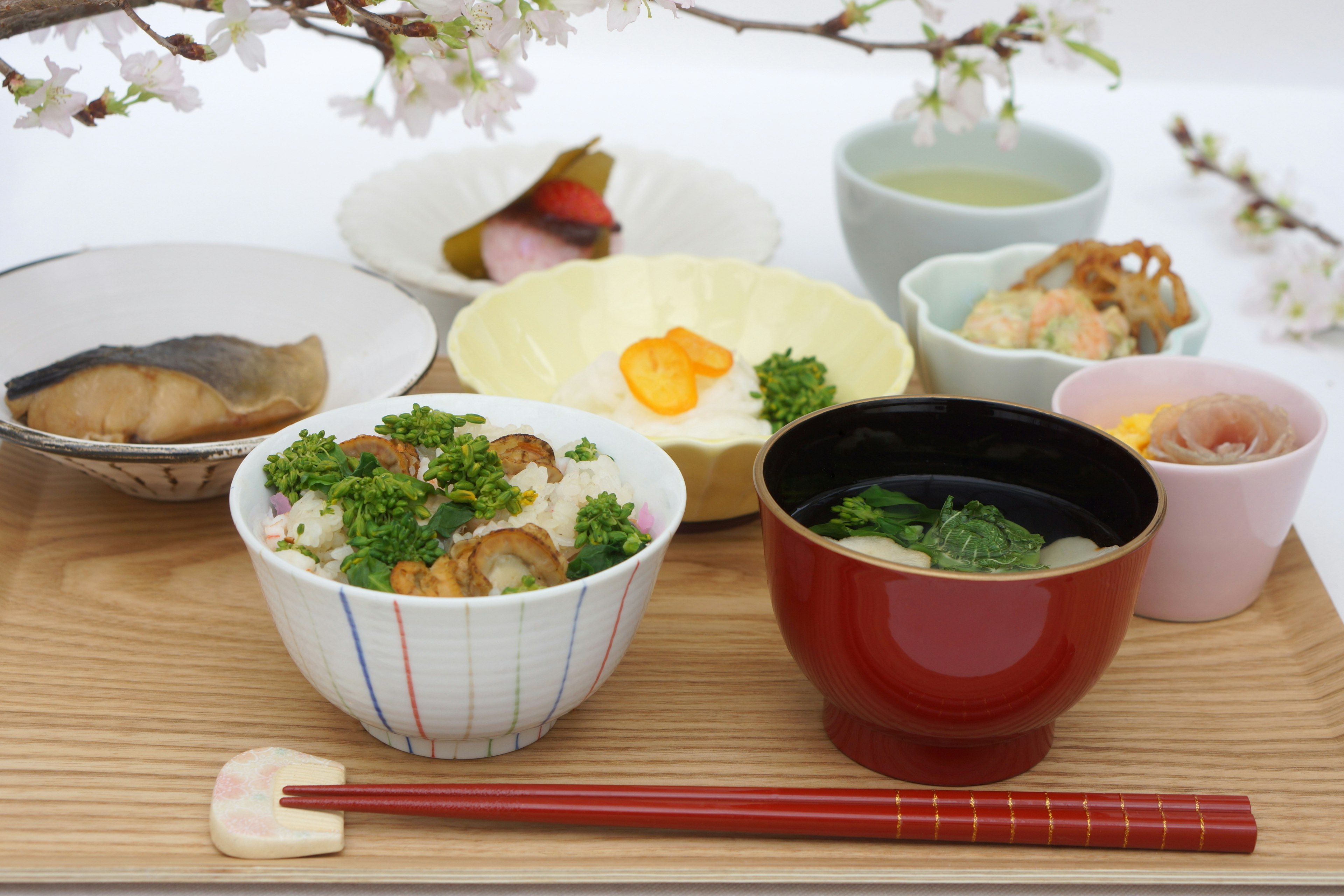 Una variedad de platos de desayuno japonés dispuestos bajo flores de cerezo