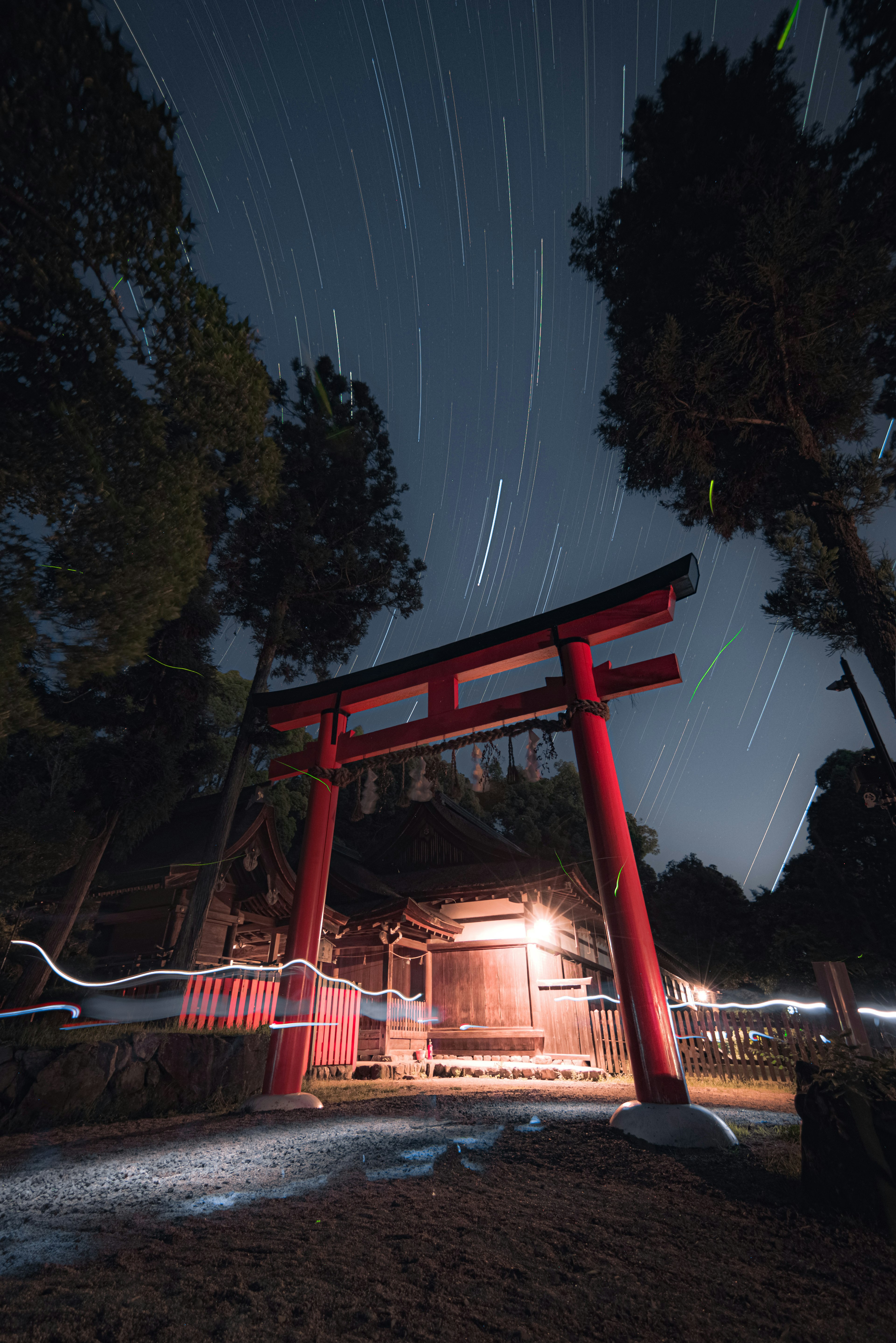 Red torii gate illuminated at night with star trails in the sky